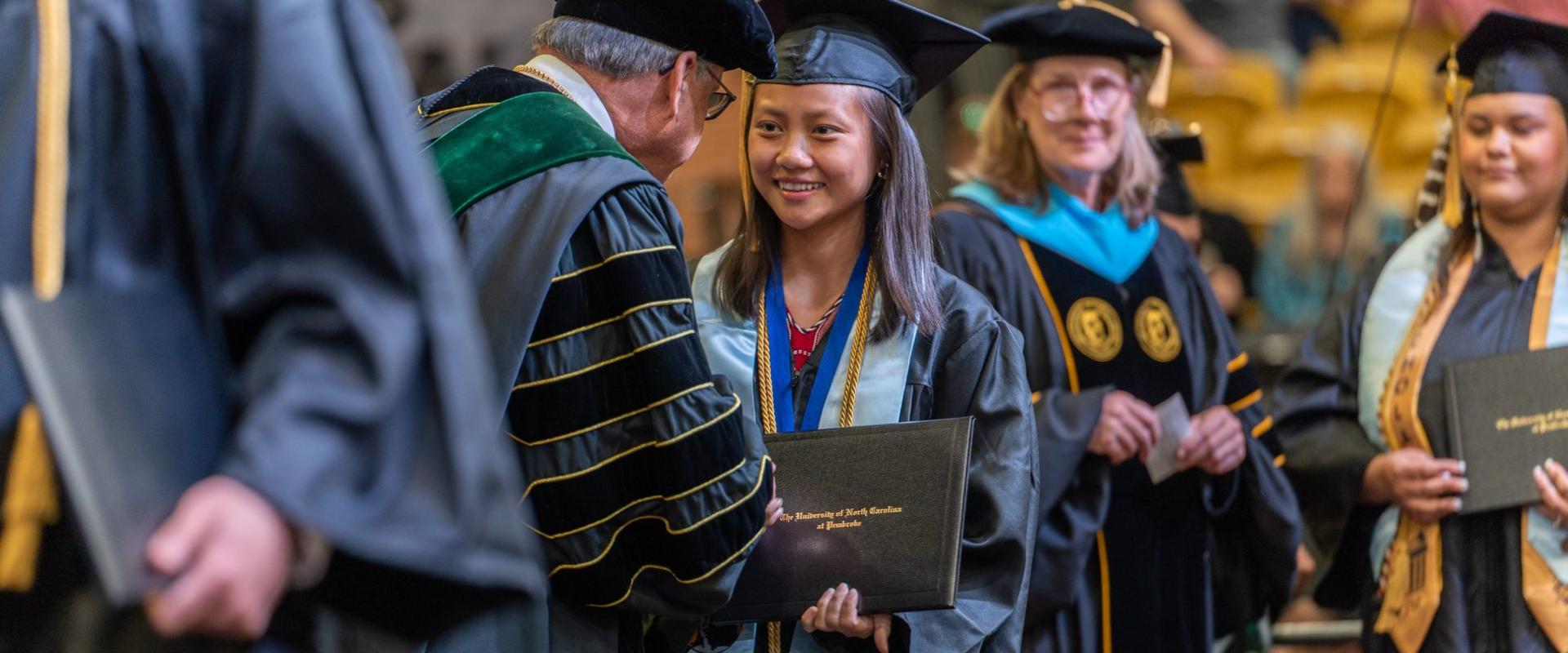 Student accepting diploma as she shakes the Chancellor's hand.