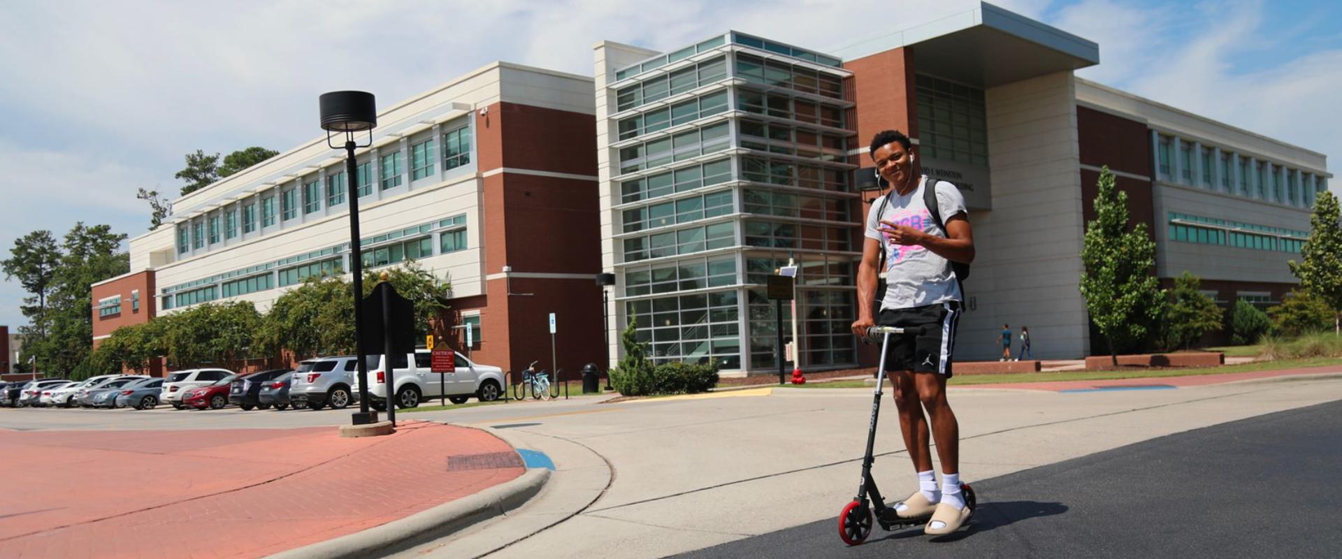 Male student rides a scooter on the UNCP campus.