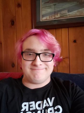 Man with glasses and pink hair smiling at the camera
