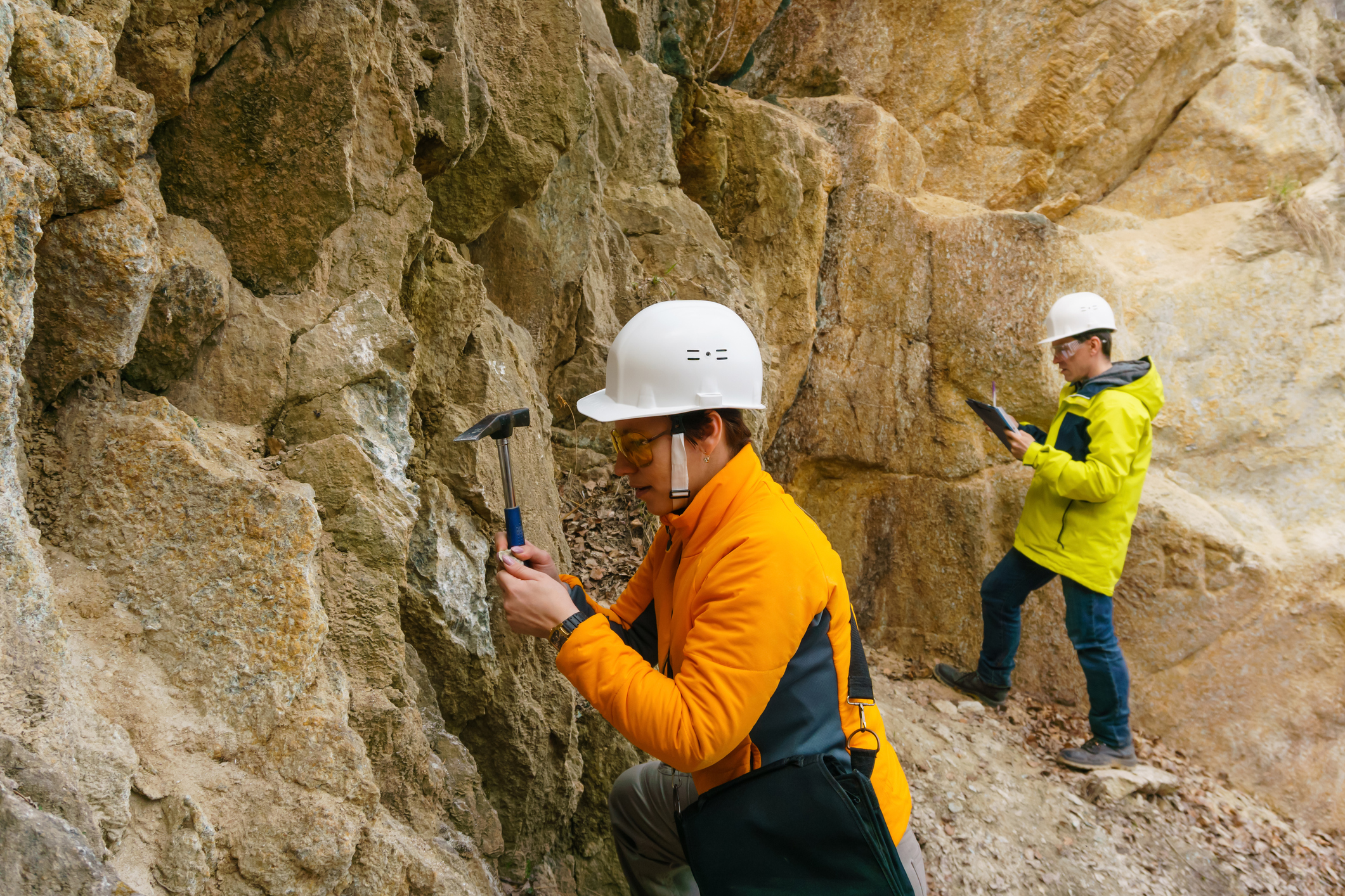 male and female geologist looking at rock on the side of mountain