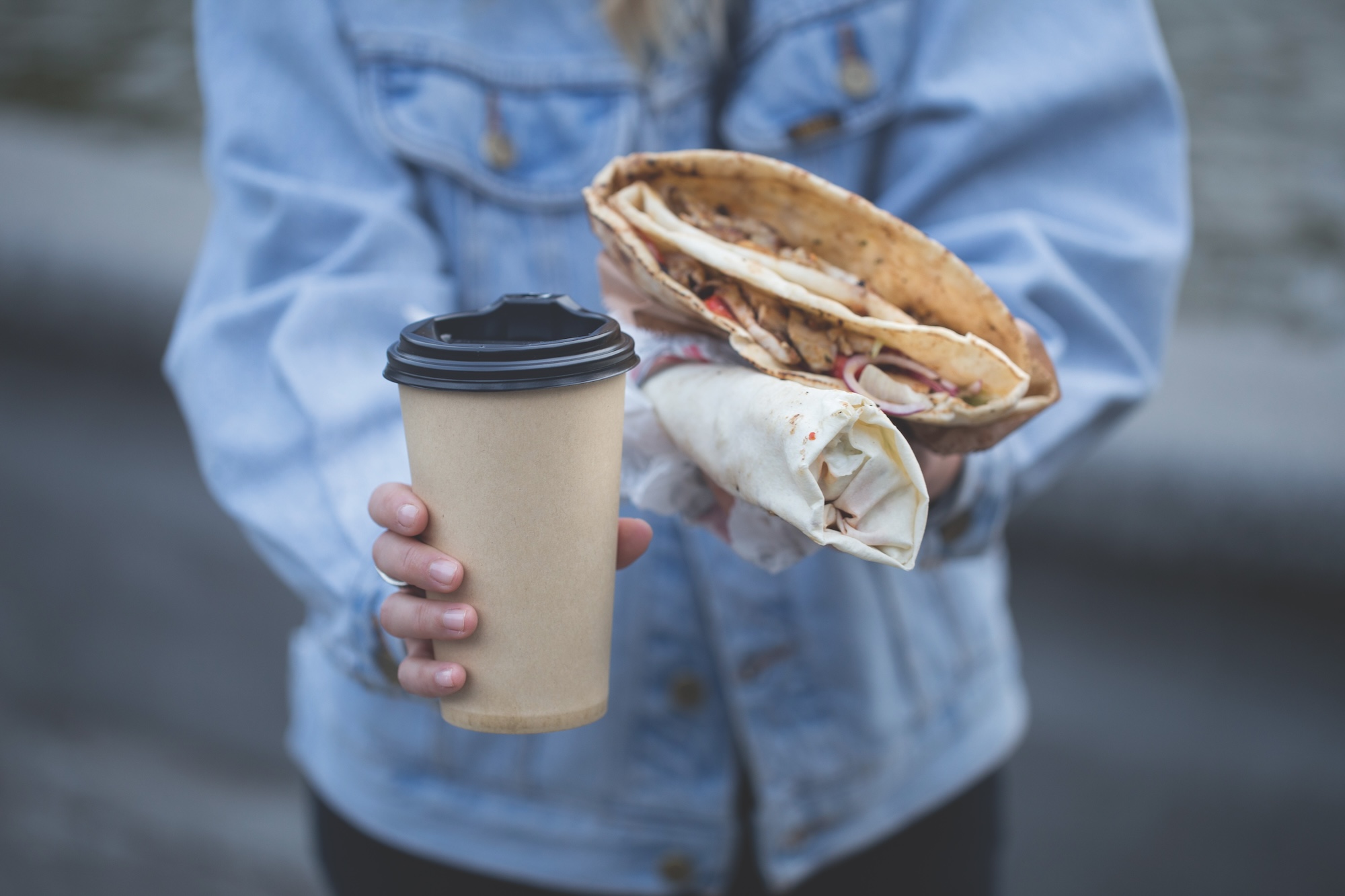 A woman holding a coffe cup and open food packaged close up