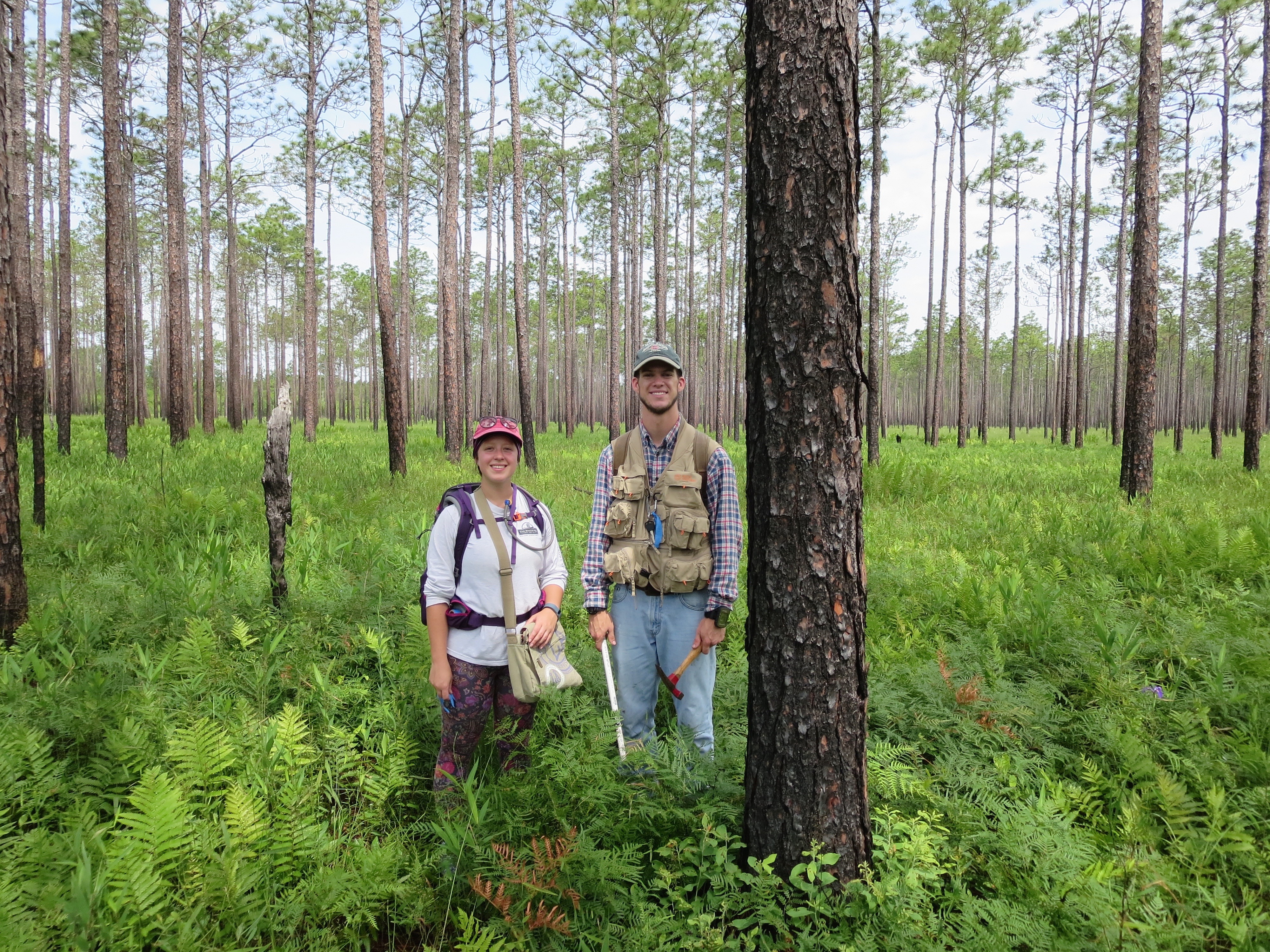 two UNCP students standing in a forest surrounded by ferns