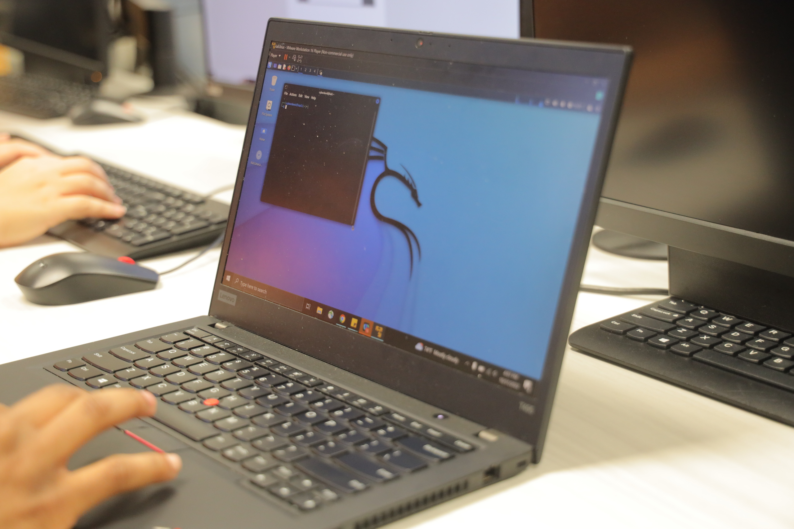 Close-up of a student using a Lenovo laptop running a cybersecurity or coding program, with other monitors and keyboards visible in a computer lab setting.