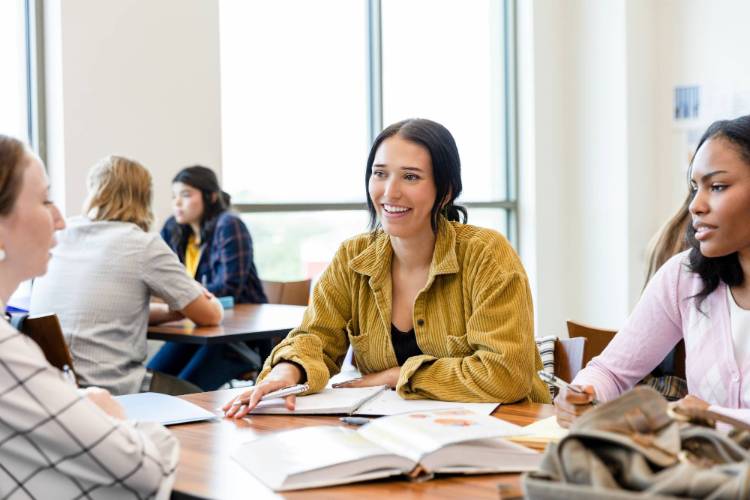 three women sitting at a circle table with a book open