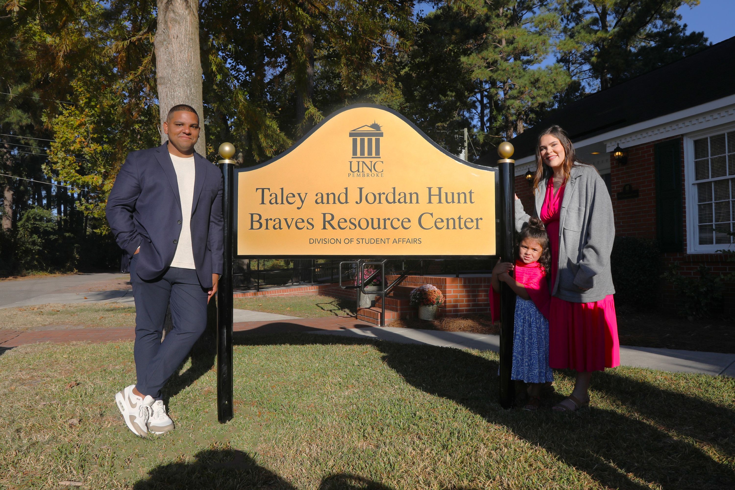 Taley and Jordan Hunt standing next to the sign with their daughter at the renaming ceremony for the Jordan and Taley Hunt Resource Center.