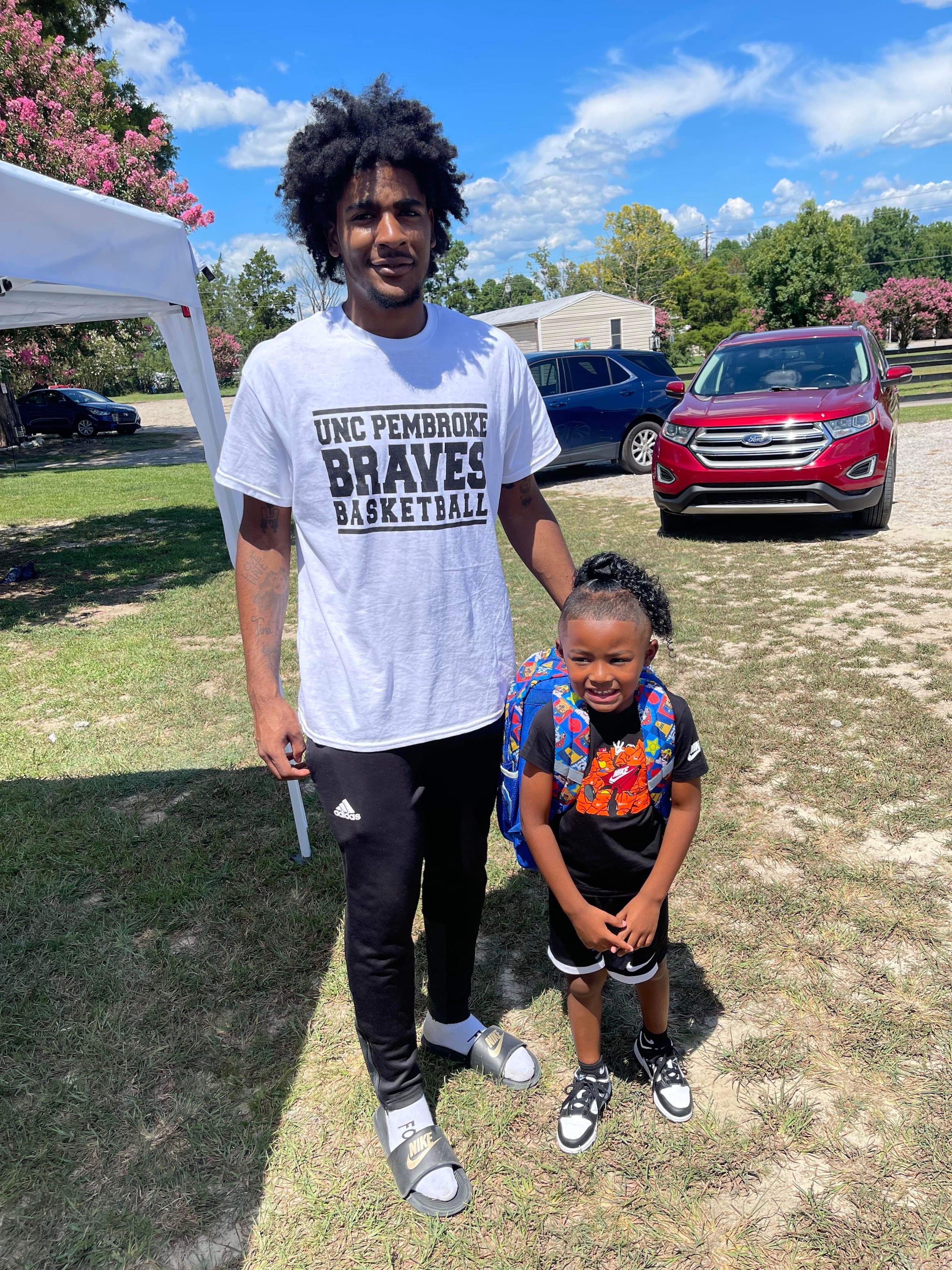 A UNCP basketball player posing with a young girl at a back to school event