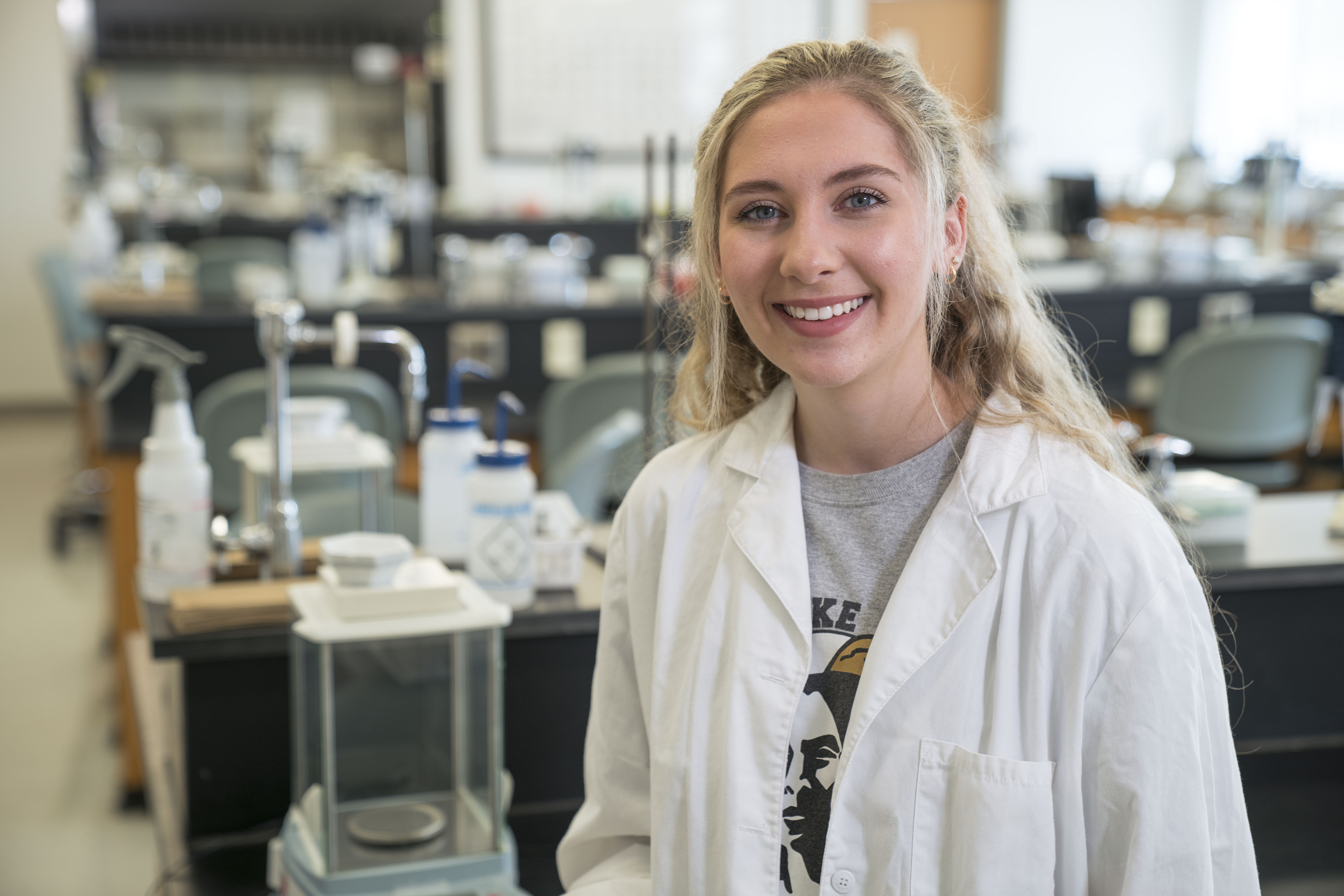 UNCP Biology alumna Lindsay Branch smiles in a lab coat in the biology lab, representing career outcomes for Biology graduates with a Biomedical emphasis.