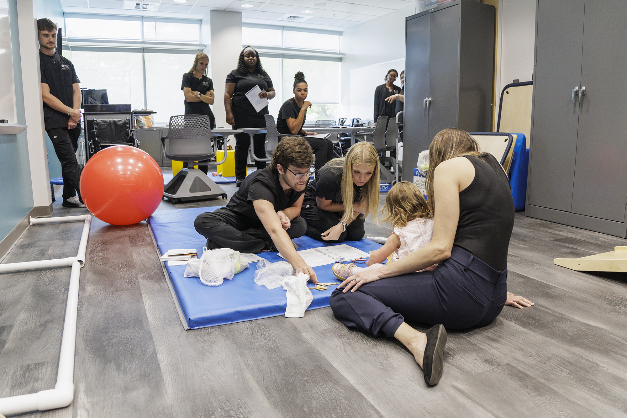 UNC Pembroke occupational therapy students work with a child and caregiver during a hands-on pediatric therapy training exercise while classmates observe in a clinical lab setting.