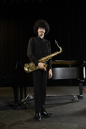 Jaylen Jones posing with his saxopohone in front of a piano on stage