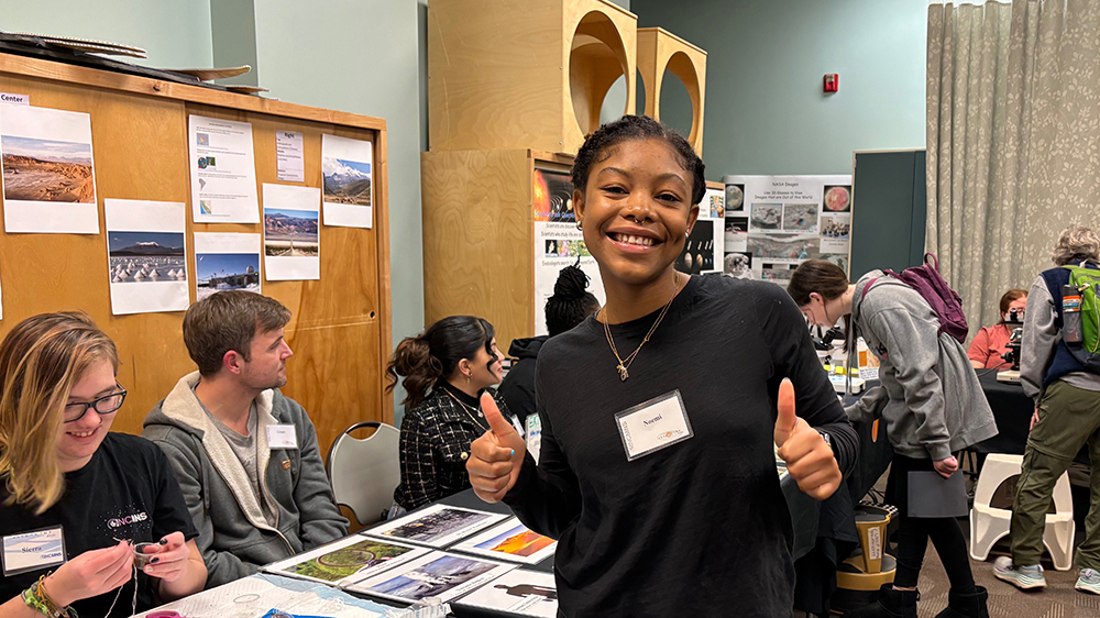UNCP student Noemi smiles and holds two thumbs up at the NCAS booth.