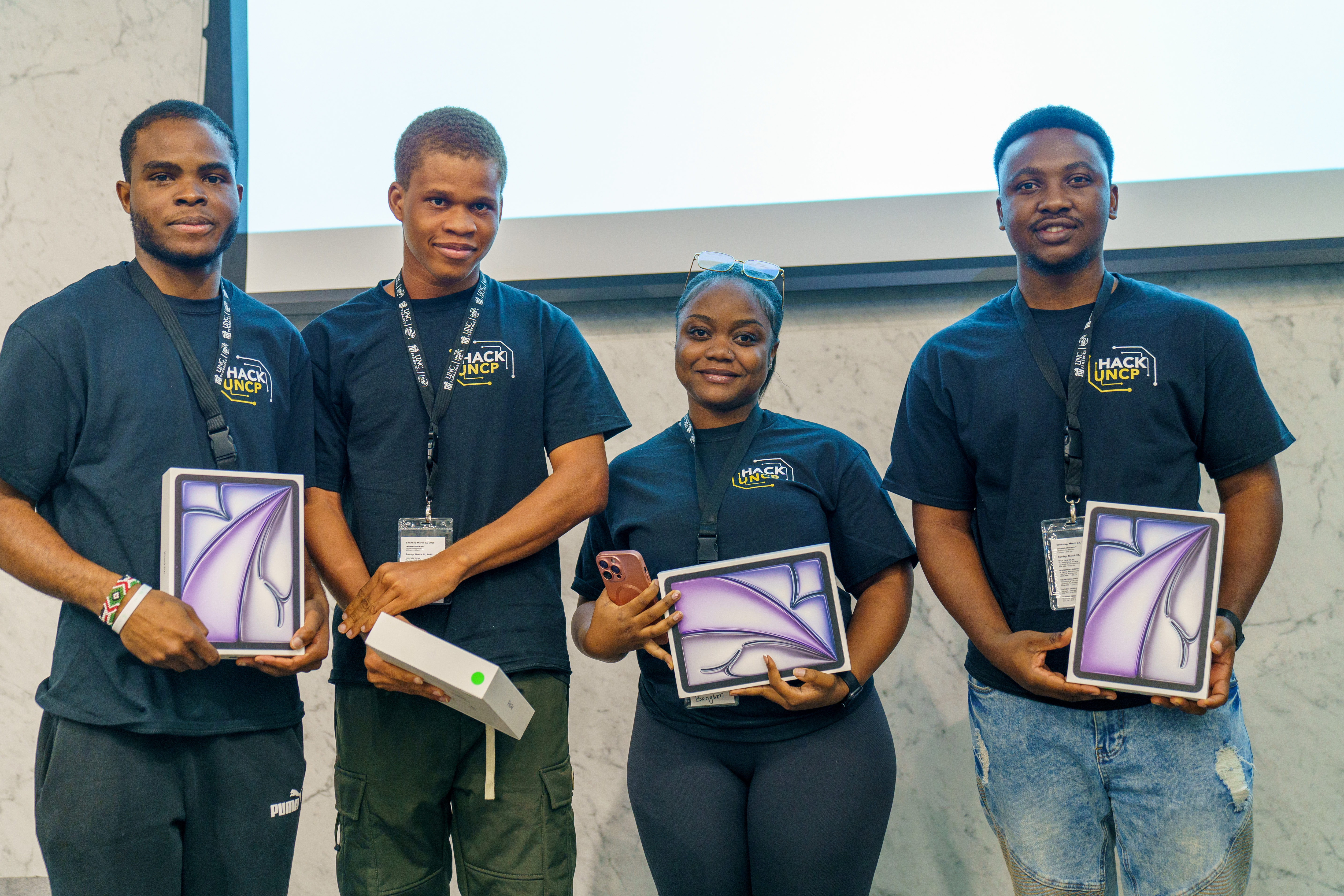four students stand with tablets as prizes for HackUNCP