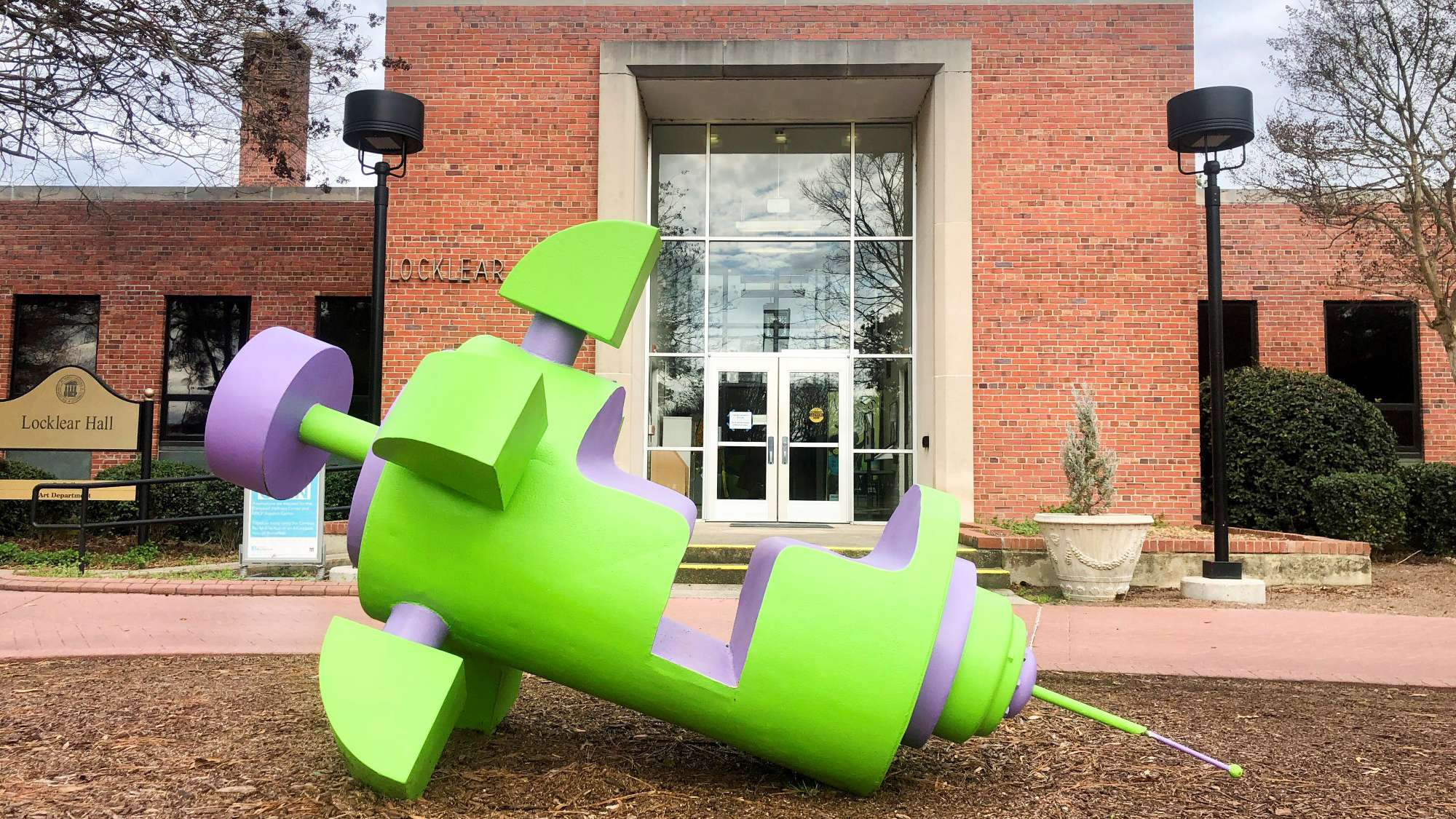 A large sculpture of a cartoonish syringe with seating for two as if it were a ride. The sculpture rests in front of Locklear Hall, home to the A.D. Gallery.