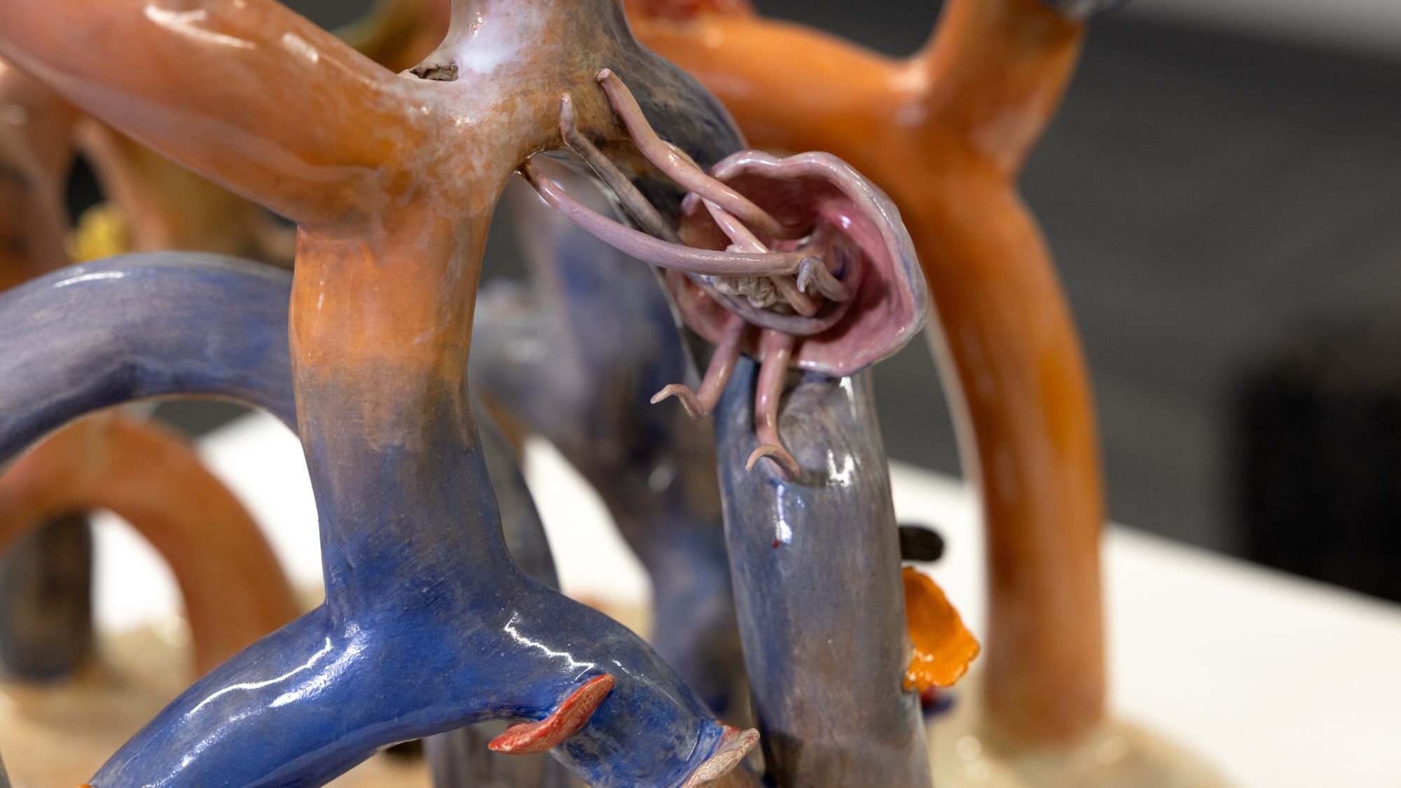 A close-up of Mia Baca’s coral sculpture shows glossy coral branches in soft orange, blue and gray tones. Nestled among the forms is a small sea creature detail, adding to the piece’s layered underwater environment.