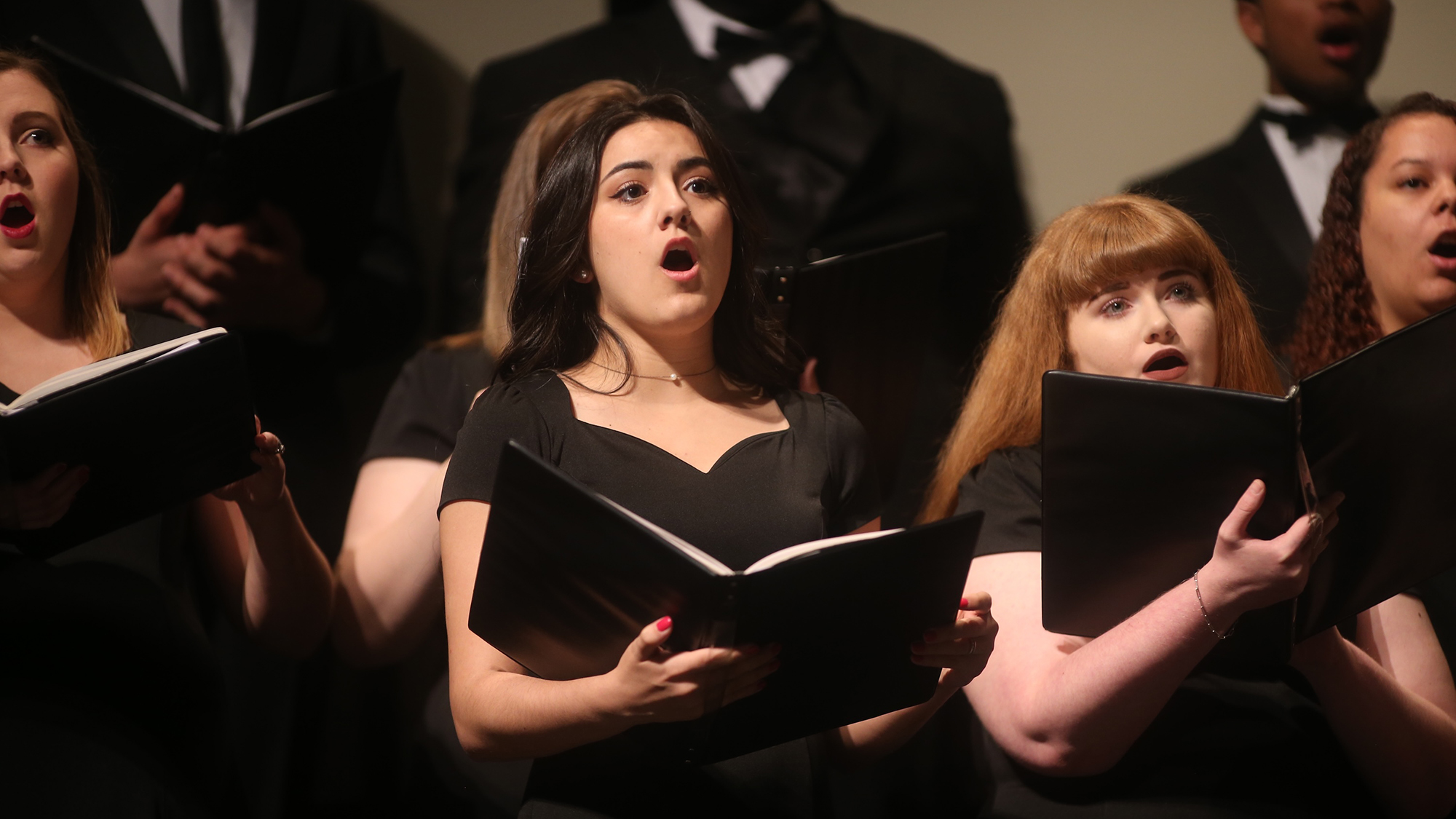 female choir singers singing while holding hymn books