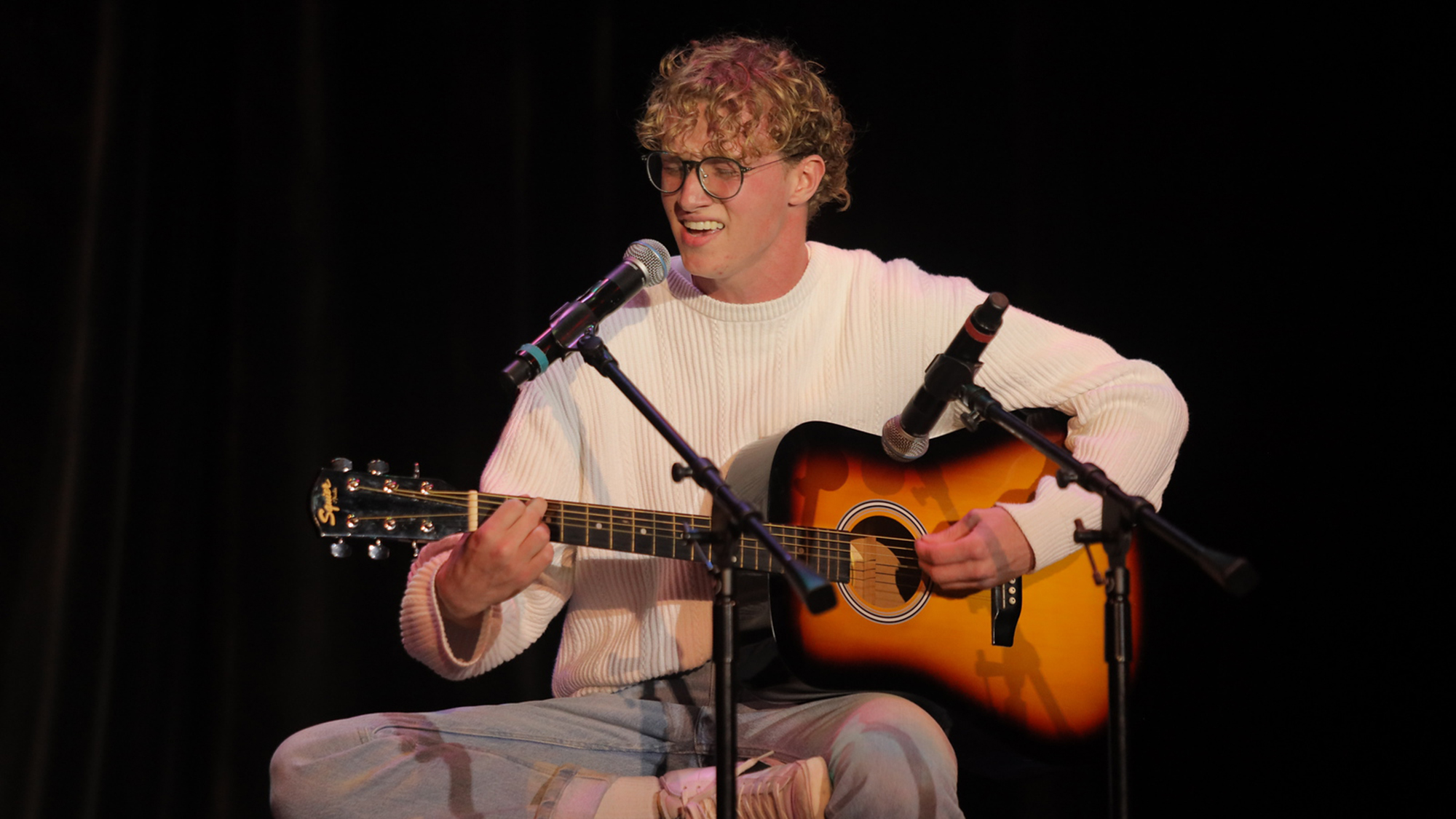 Student performing on stage while singing and playing acoustic guitar at UNC Pembroke, highlighting student in the performing arts.