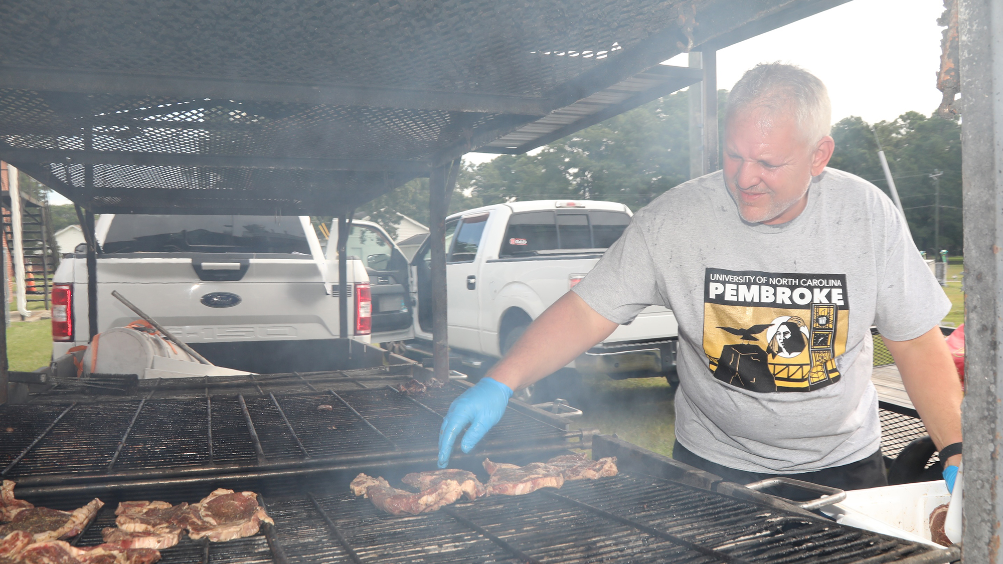 male volunteer tends steaks on a large outdoor grill