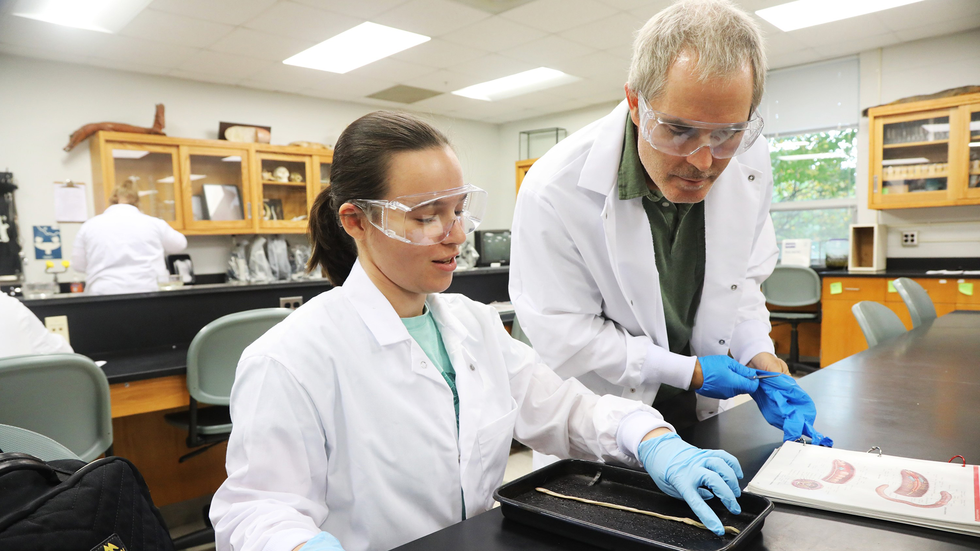Professor John Roe looks over the shoulder of a female zoology student dissecting a worm in a science lab at UNC Pembroke.
