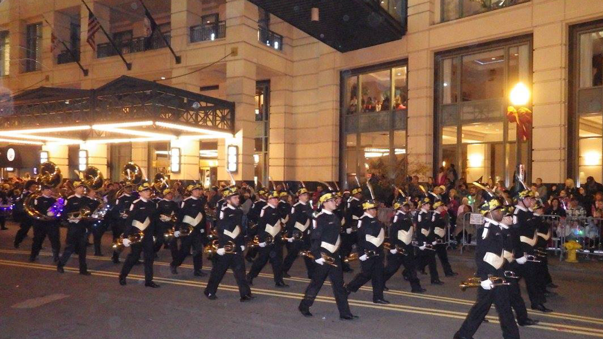 band marching along street at night in front of building while playing
