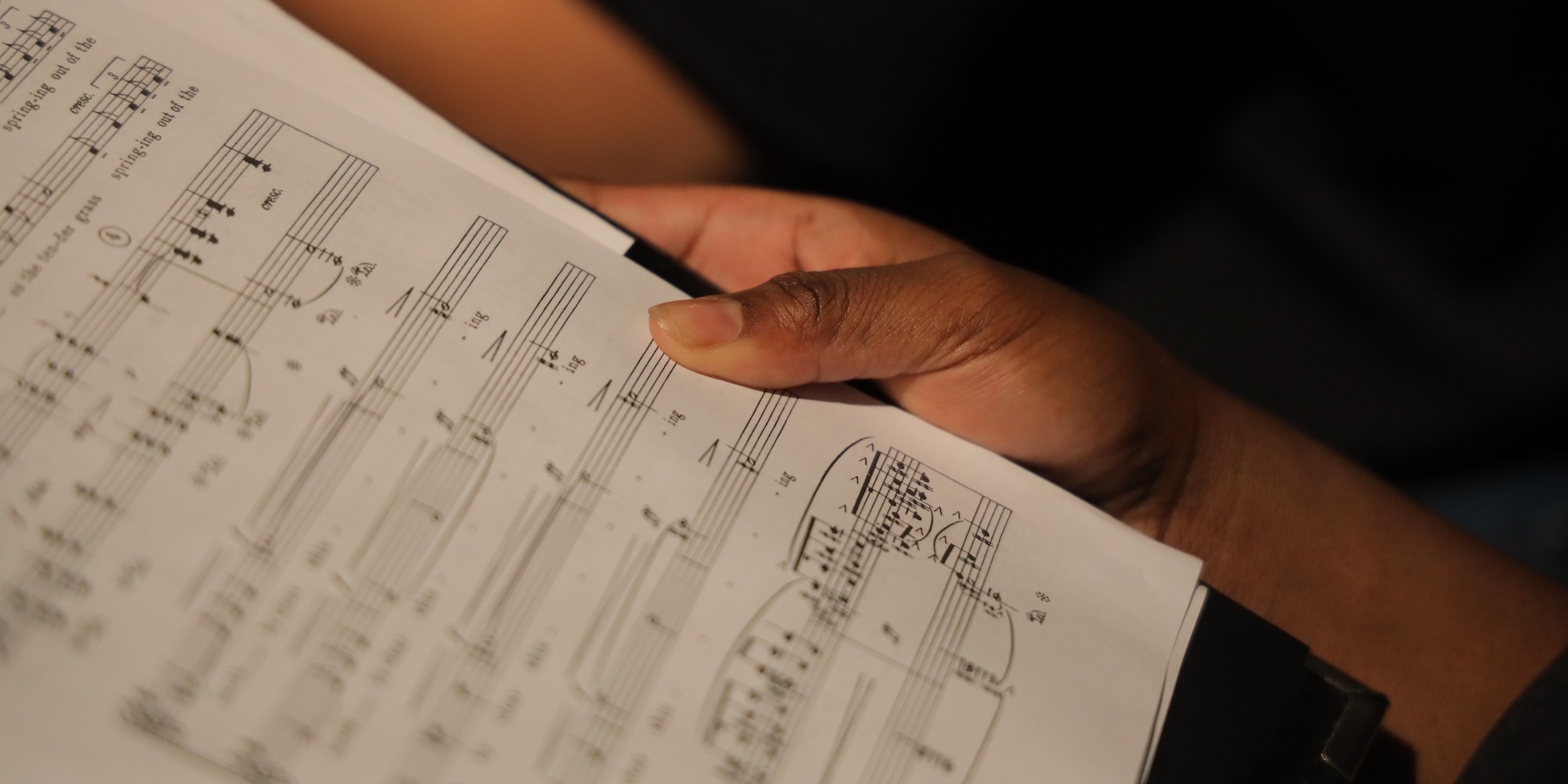 Hands holding sheet music in dramatic lighting.