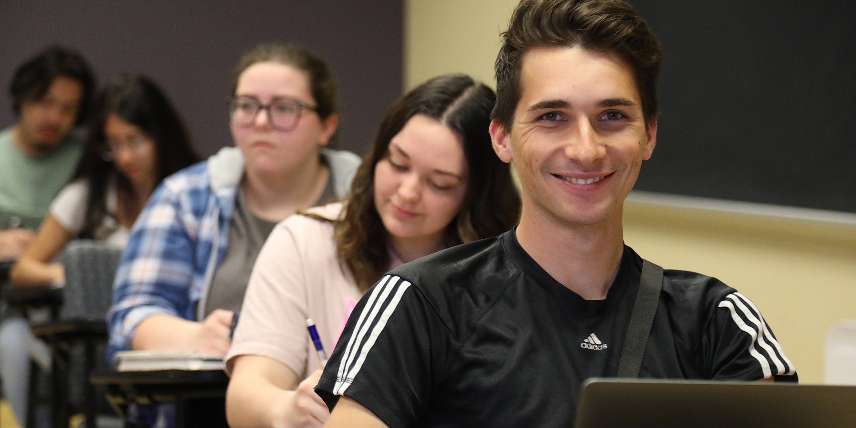 Psychology student at his desk in psychology class, smiling at the camera at UNC Pembroke.