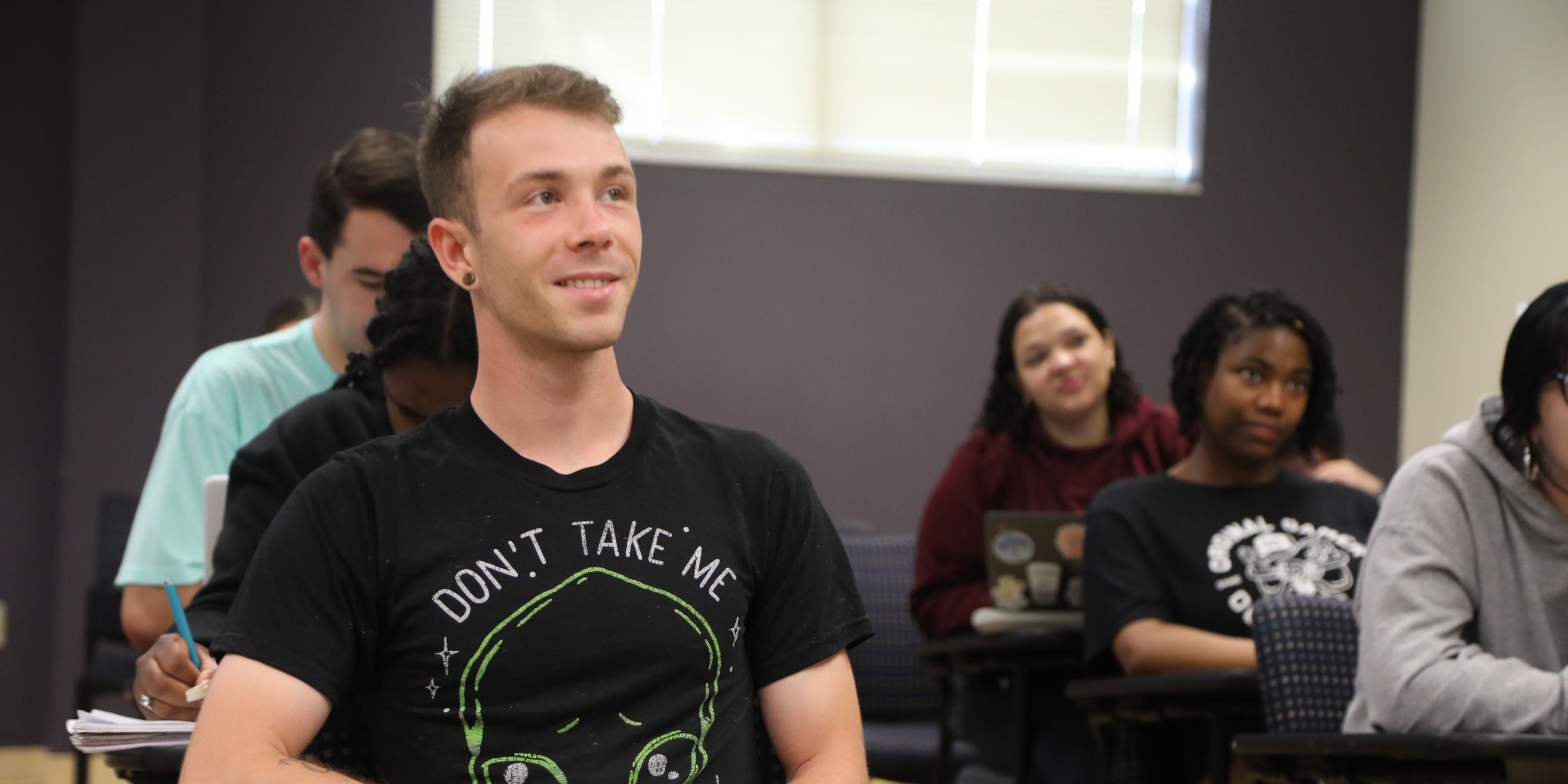 Smiling student at a desk in a classroom surounded by other students