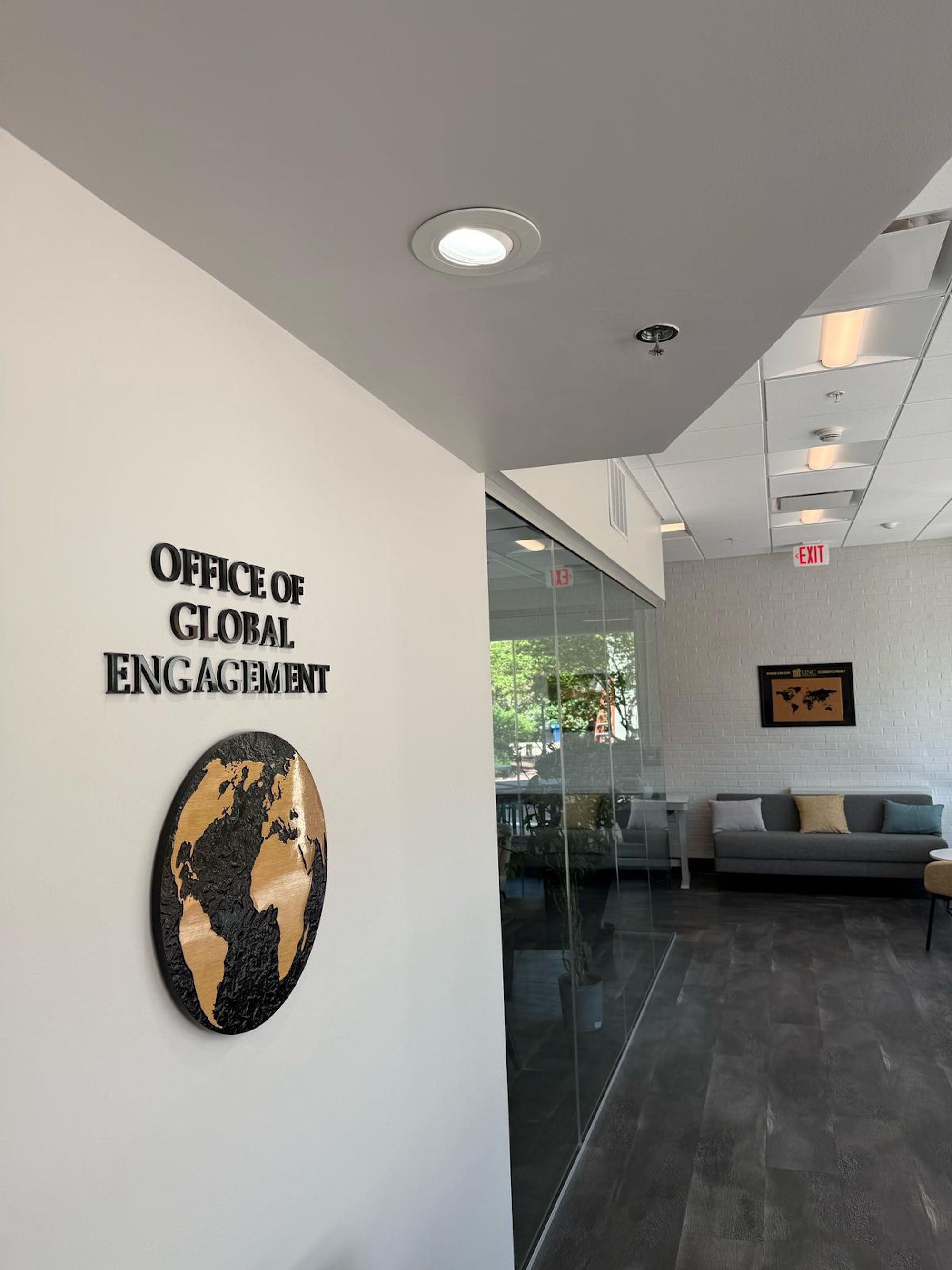 The entrance to the UNCP Office of Global Engagement, featuring a wall sign and decorative globe artwork in a modern office lobby.
