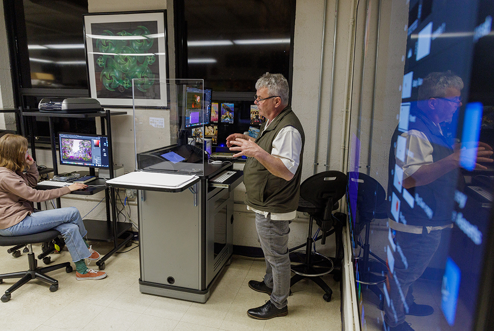 Professor in front of a large monitor gesturing and talking with a digital arts class at UNC Pembroke.
