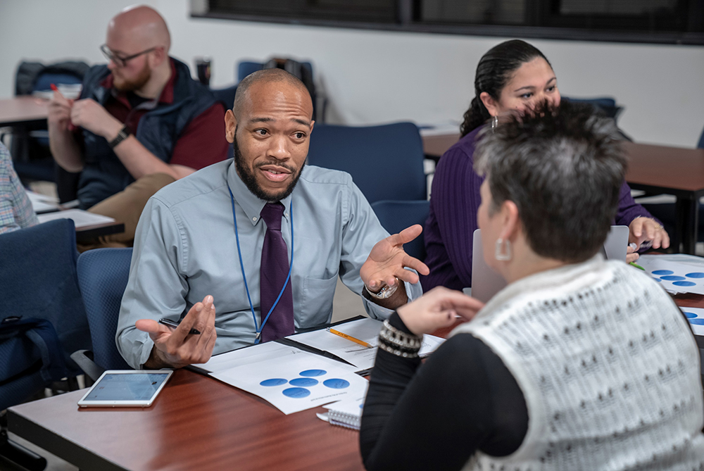 Male grad student talking with a non-traditional female at a table in the classroom at UNC Pembroke.