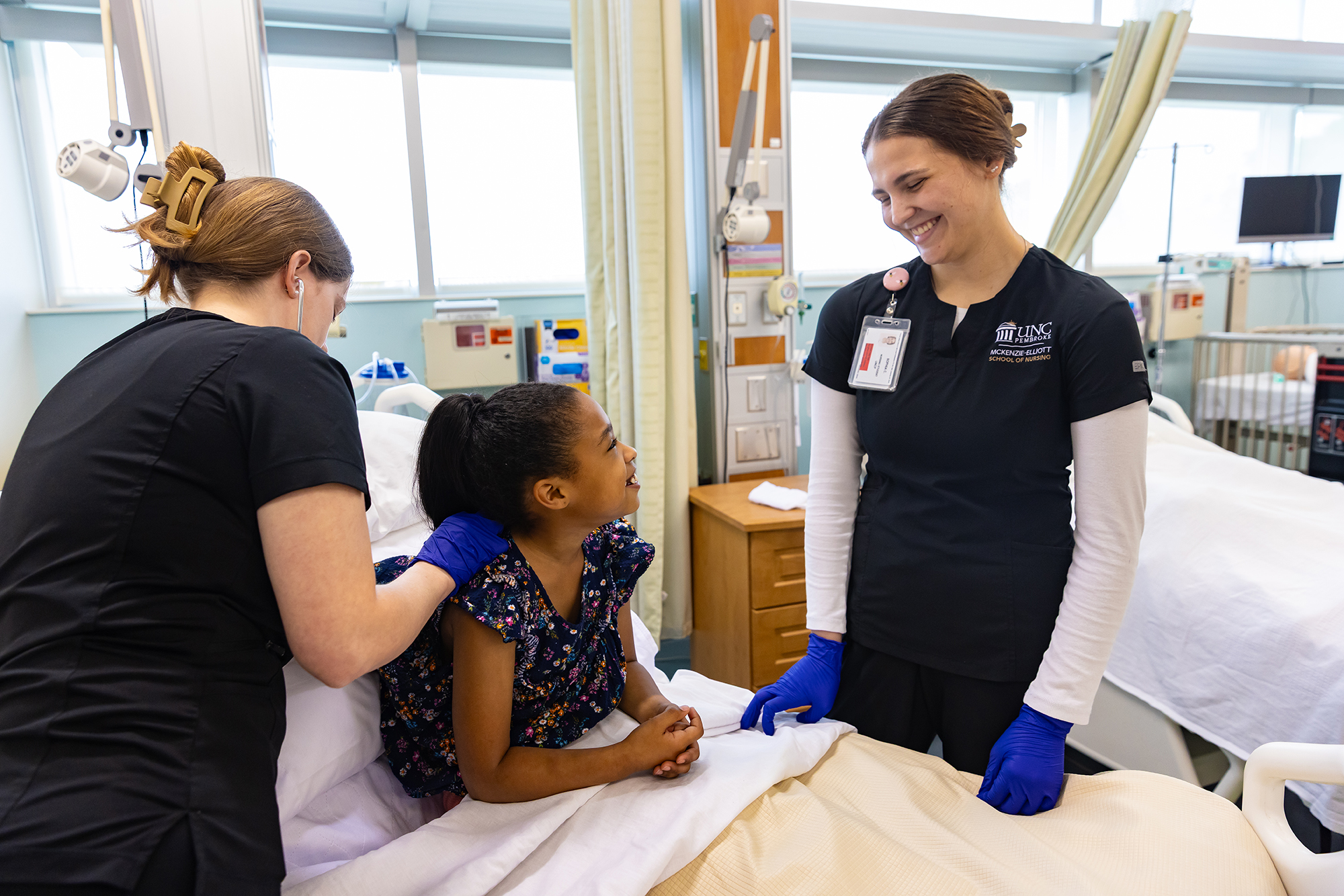 female UNCP student in nursing attire with a child patient
