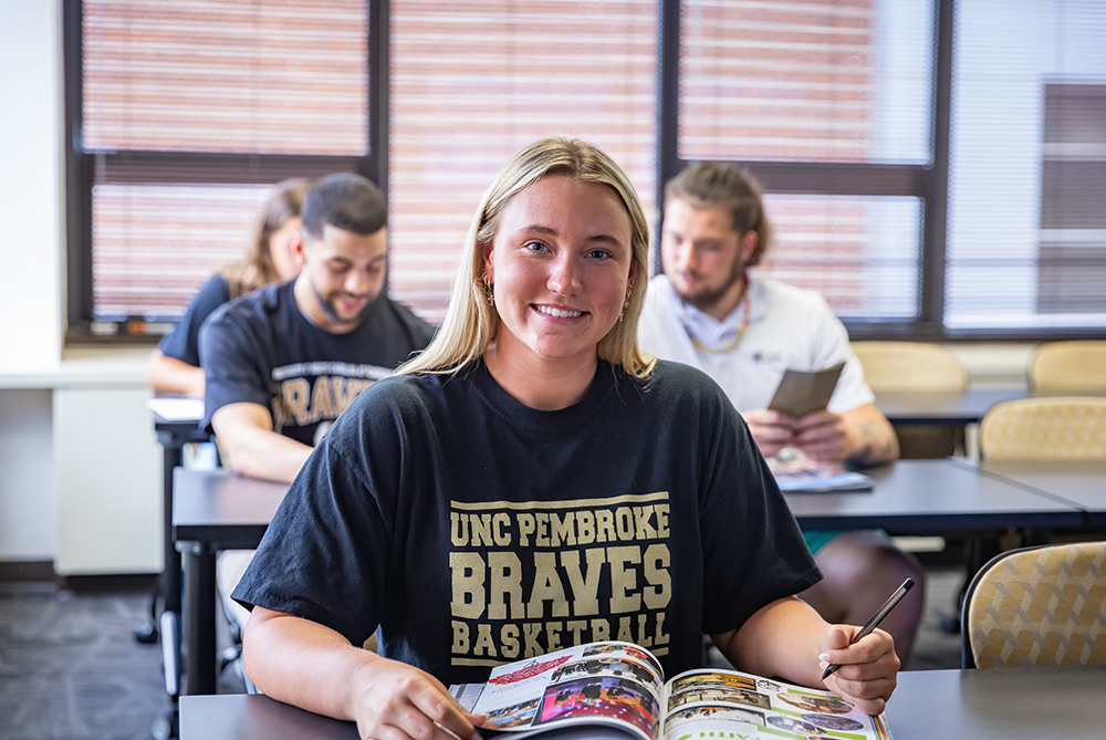 female student at desk annotating text book and smiling at camera
