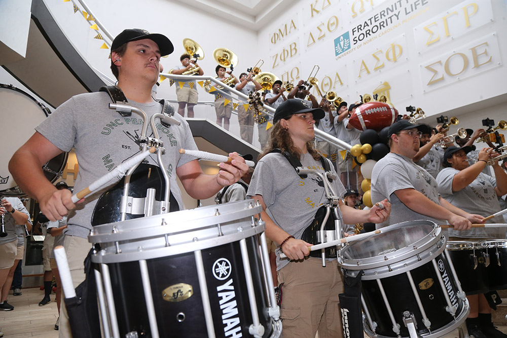 UNCP marching band members holding instruments standing inside the Chavis Student Center at UNC Pembroke (UNCP).