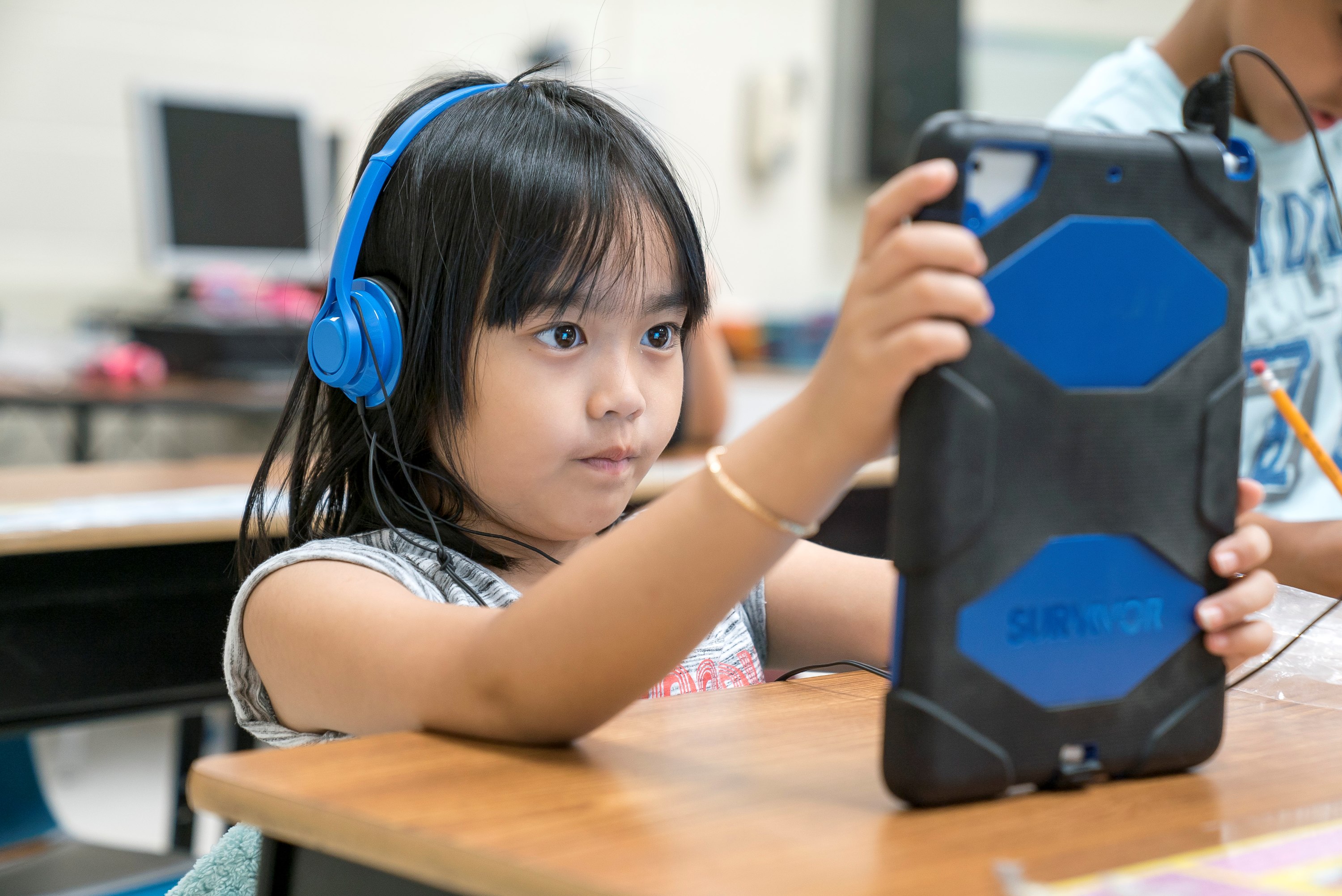 Young elementary school student wearing headphones and reading an iPad.