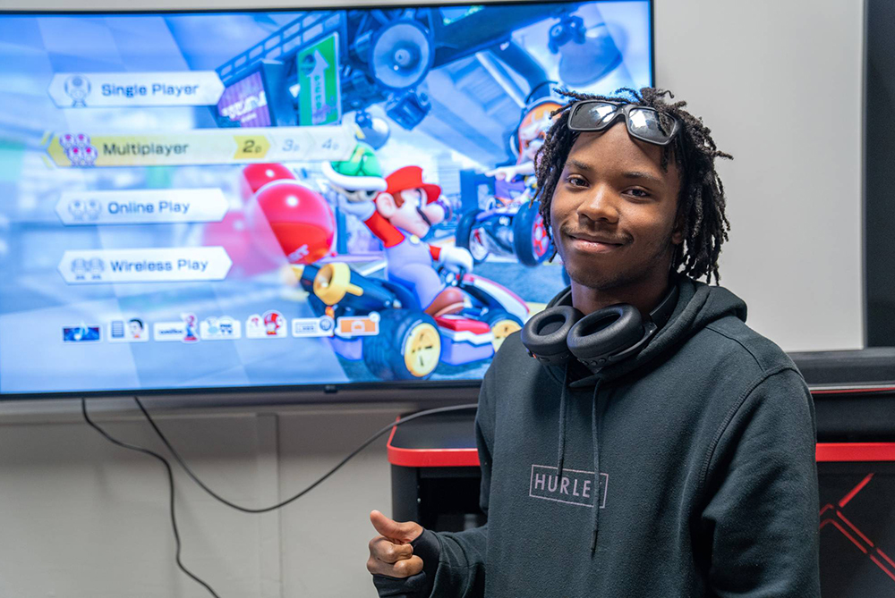 young man in front of large screen displaying Mario Kart game in progress