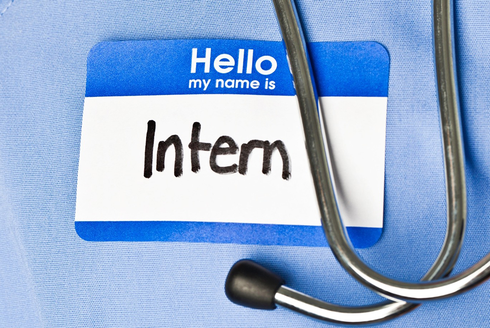 Close-up of a stethoscope and a name badge reading ‘Hello my name is Intern' on blue medical scrubs.
