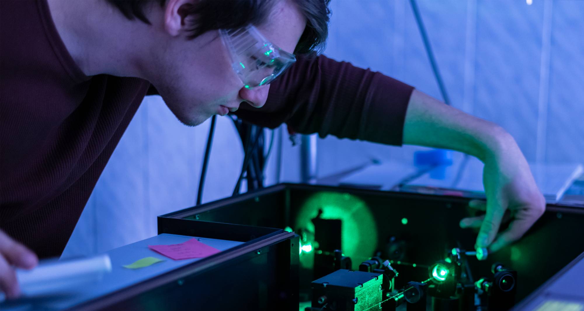 male student wearing googles inspecting science equipment in a physics lab