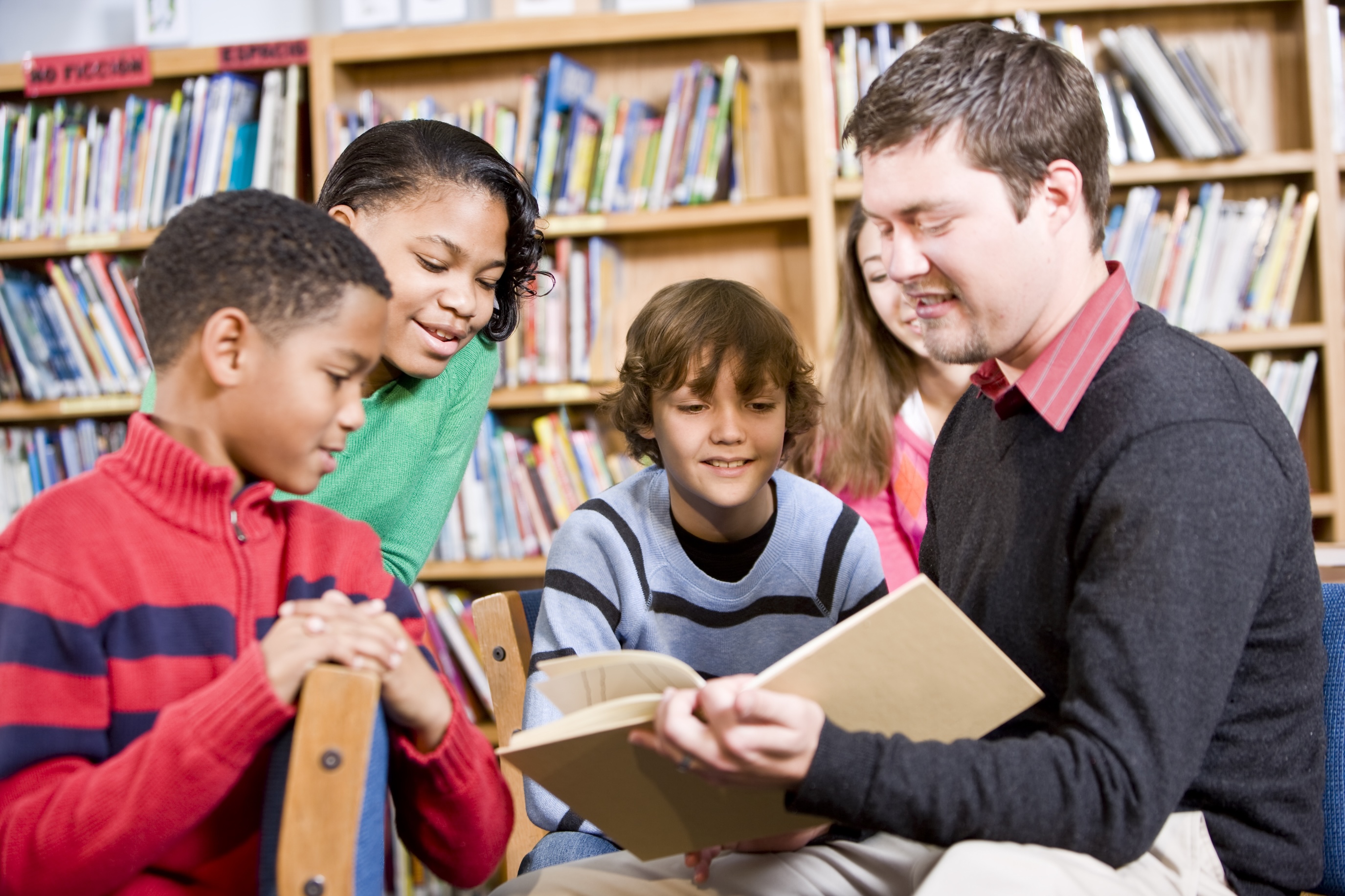 male teacher reading with students in library