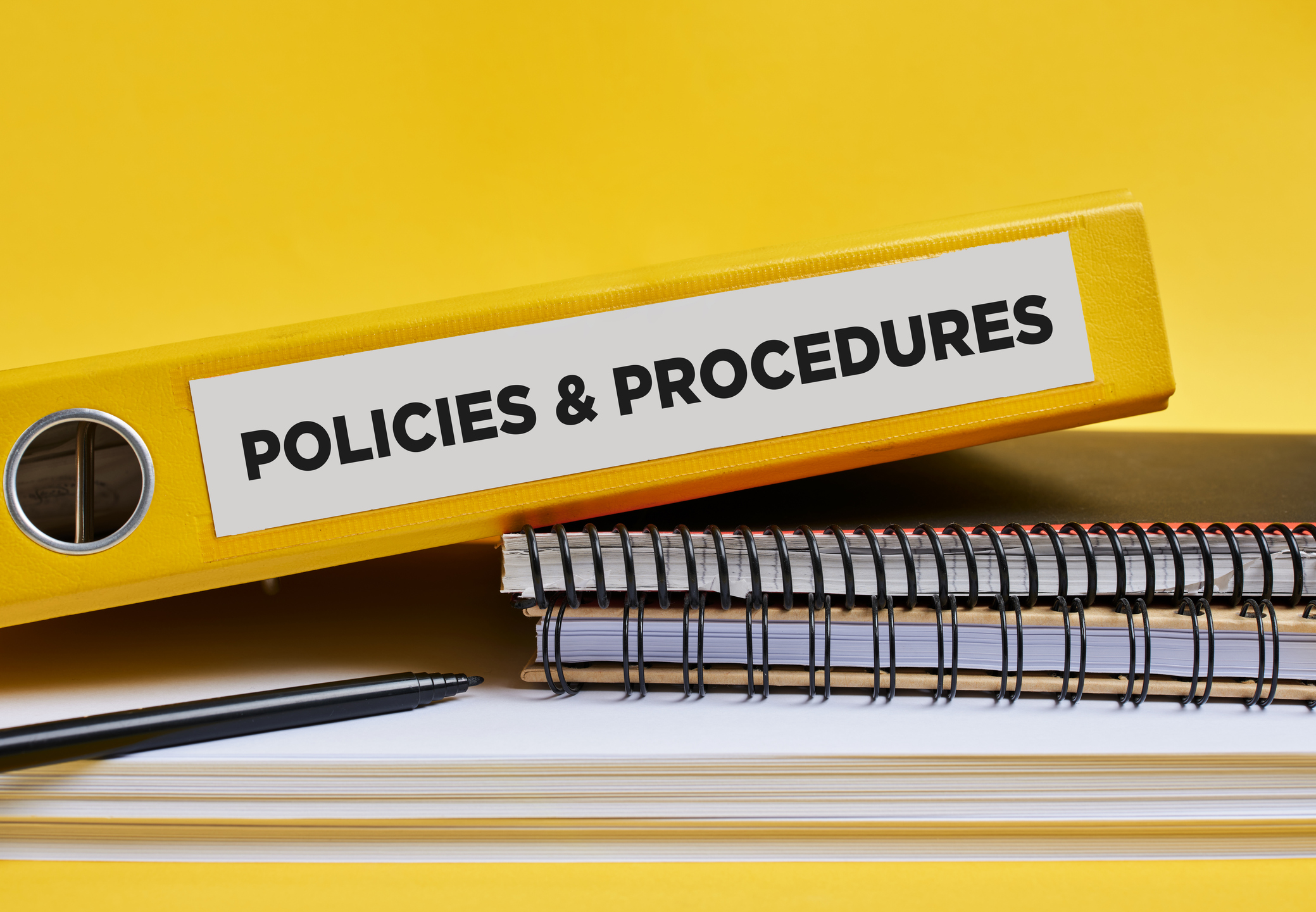 Policies and procedures written on the label of a yellow binder on the office desk.