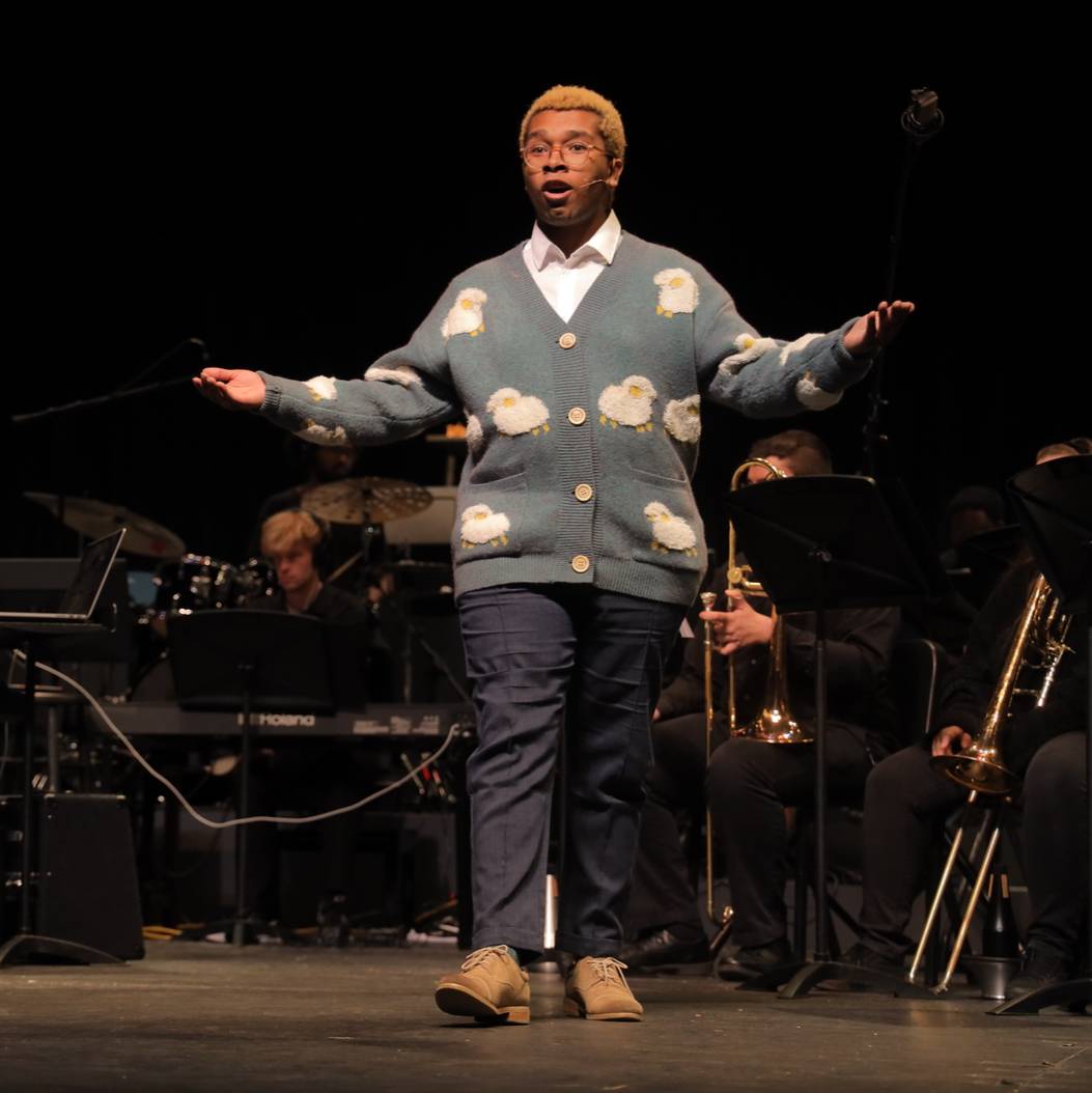 Vocal soloist performing on stage in front of a live band during a musical theatre concert at UNC Pembroke, showcasing talent and collaboration in the university’s music and performing arts programs.