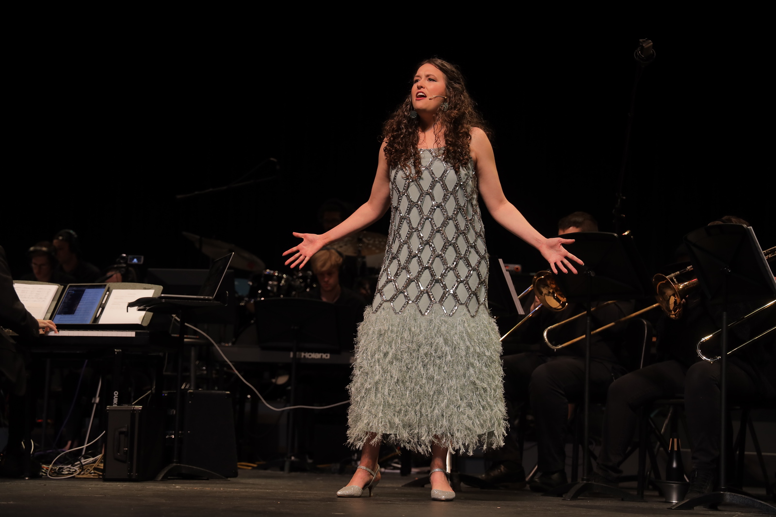 Female soloist performing passionately on stage with a live band during a musical theatre concert at UNC Pembroke, wearing a formal costume and engaging the audience with expressive vocals.
