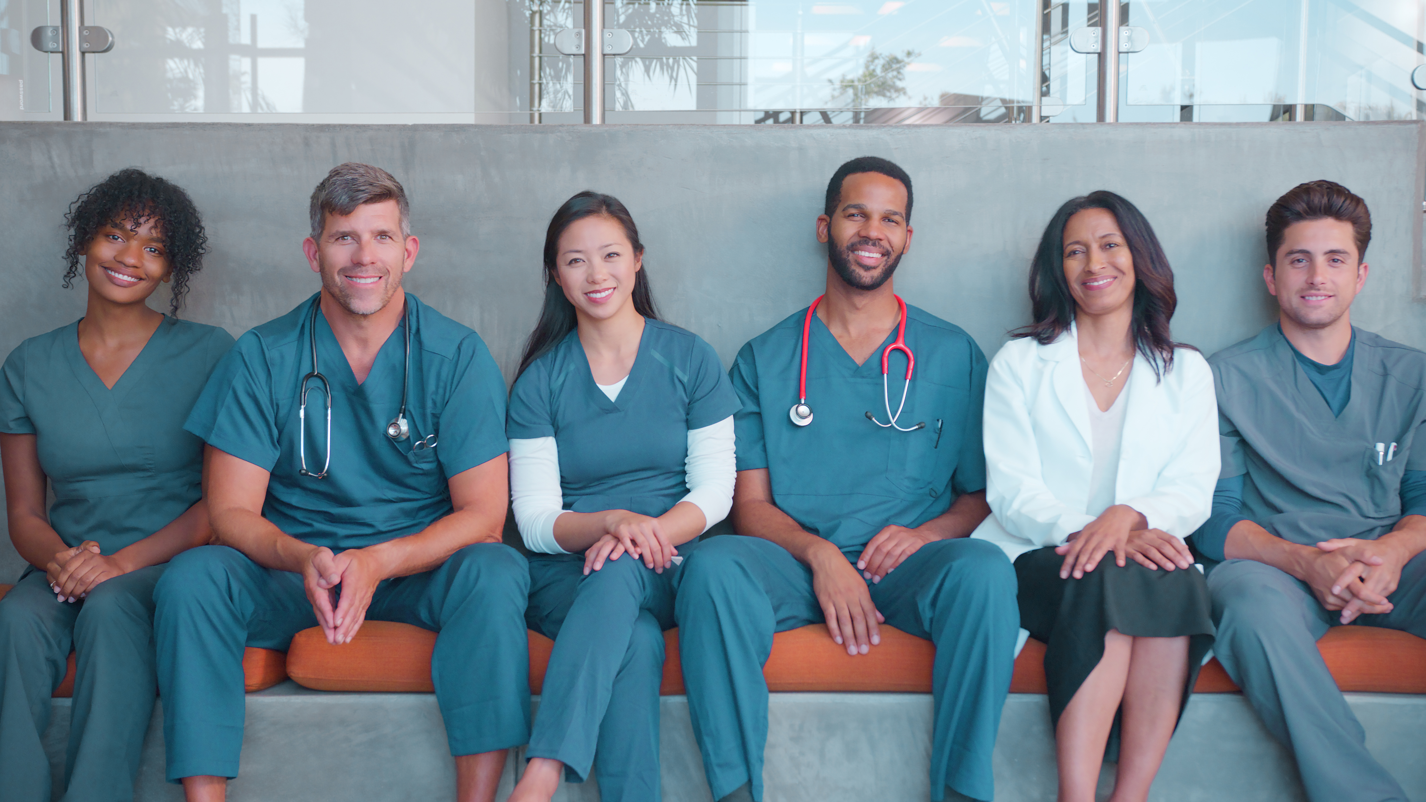 smiling nurses sitting on a bench inside of a hospital posing for a picture in scrubs