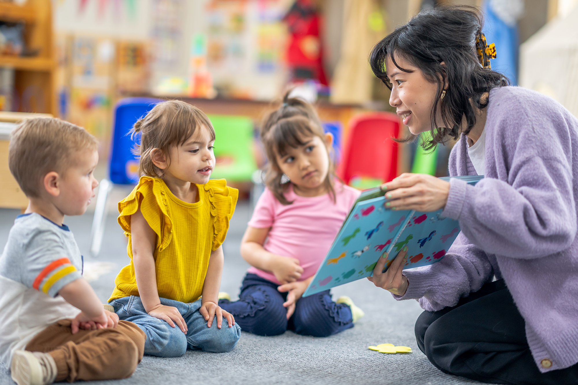 preschool teacher reading a book on the floor with young children