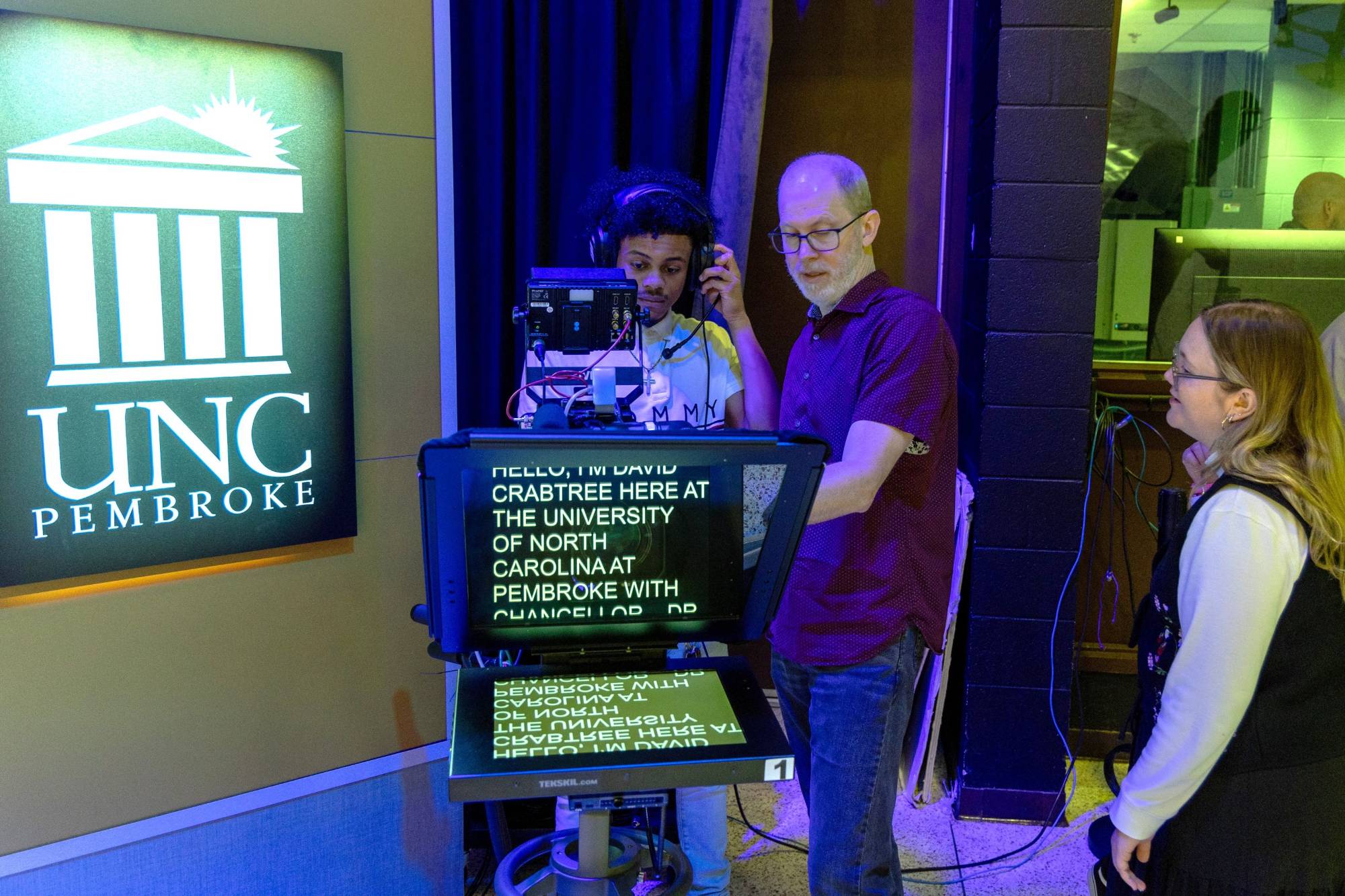 Professor Dollard instructs a black male student in using a TV studio camera while a white female student looks on in the Mass Communication TV Studio at UNC Pembroke.