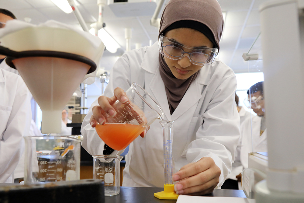 female student pours liquid from a glass container in a chemistry lab a UNC Pembroke