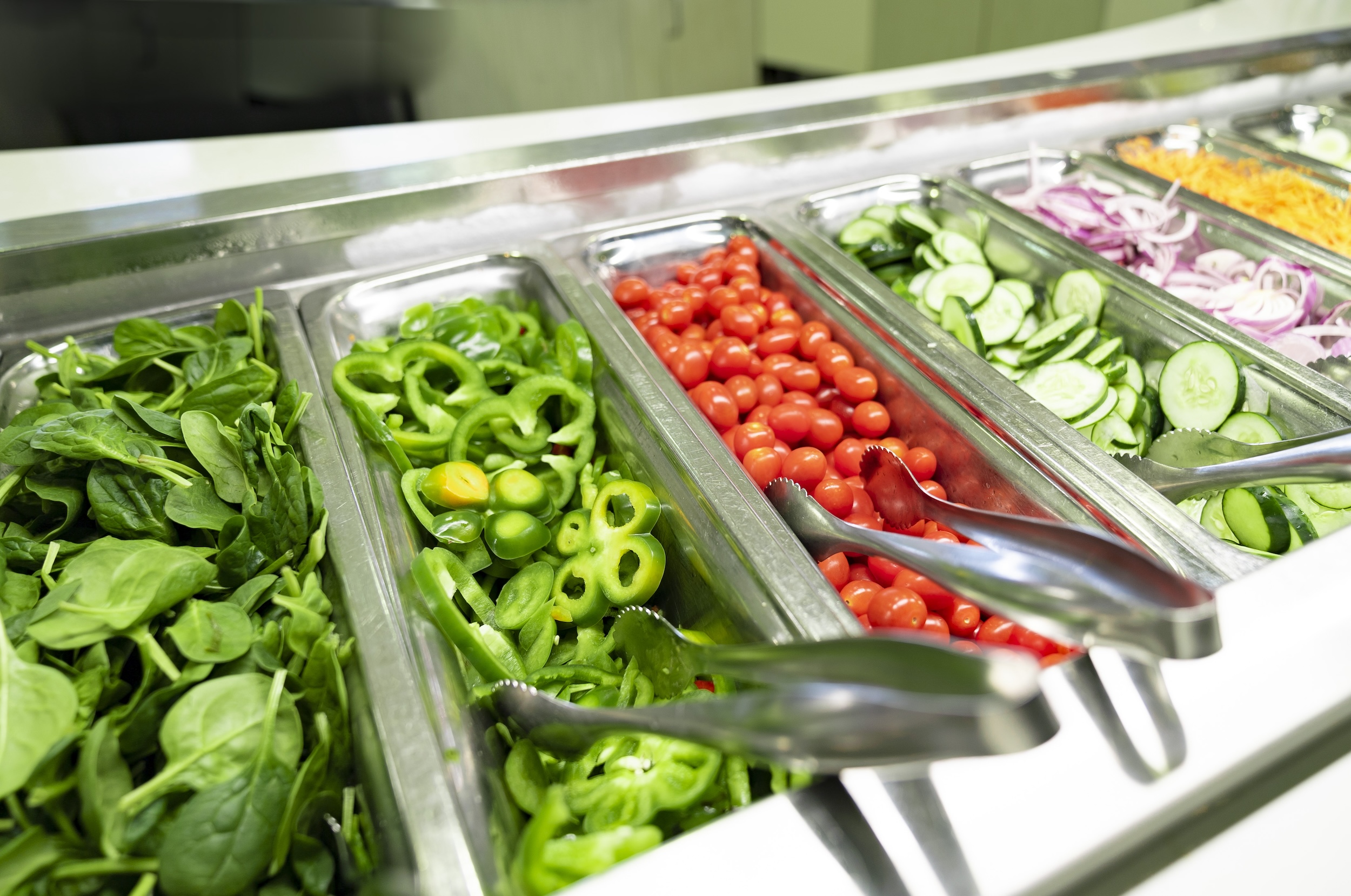 spinach peppers tomatoes cucumbers with tongs in them