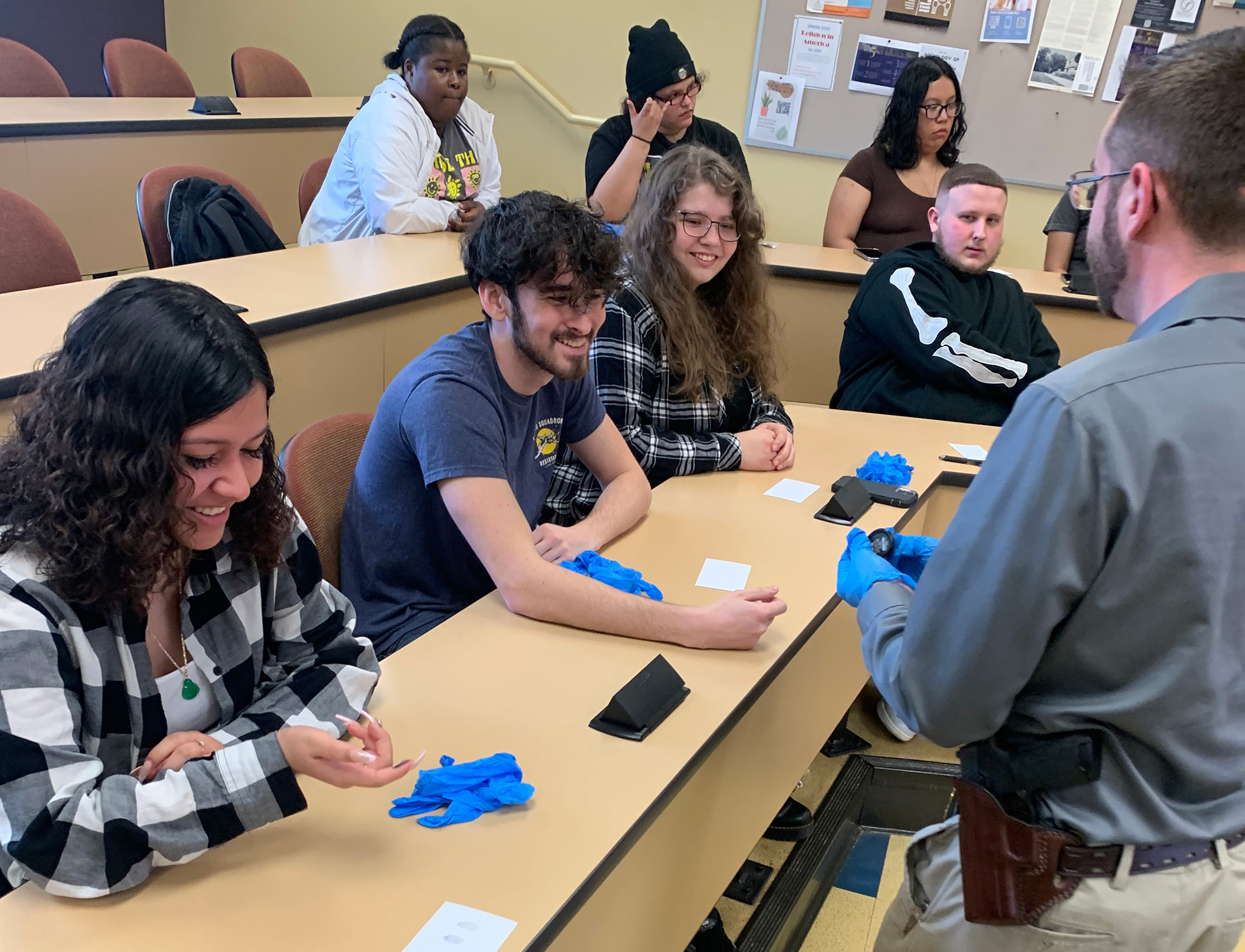 A group of students sit in a classroom while a law enforcement officer presents