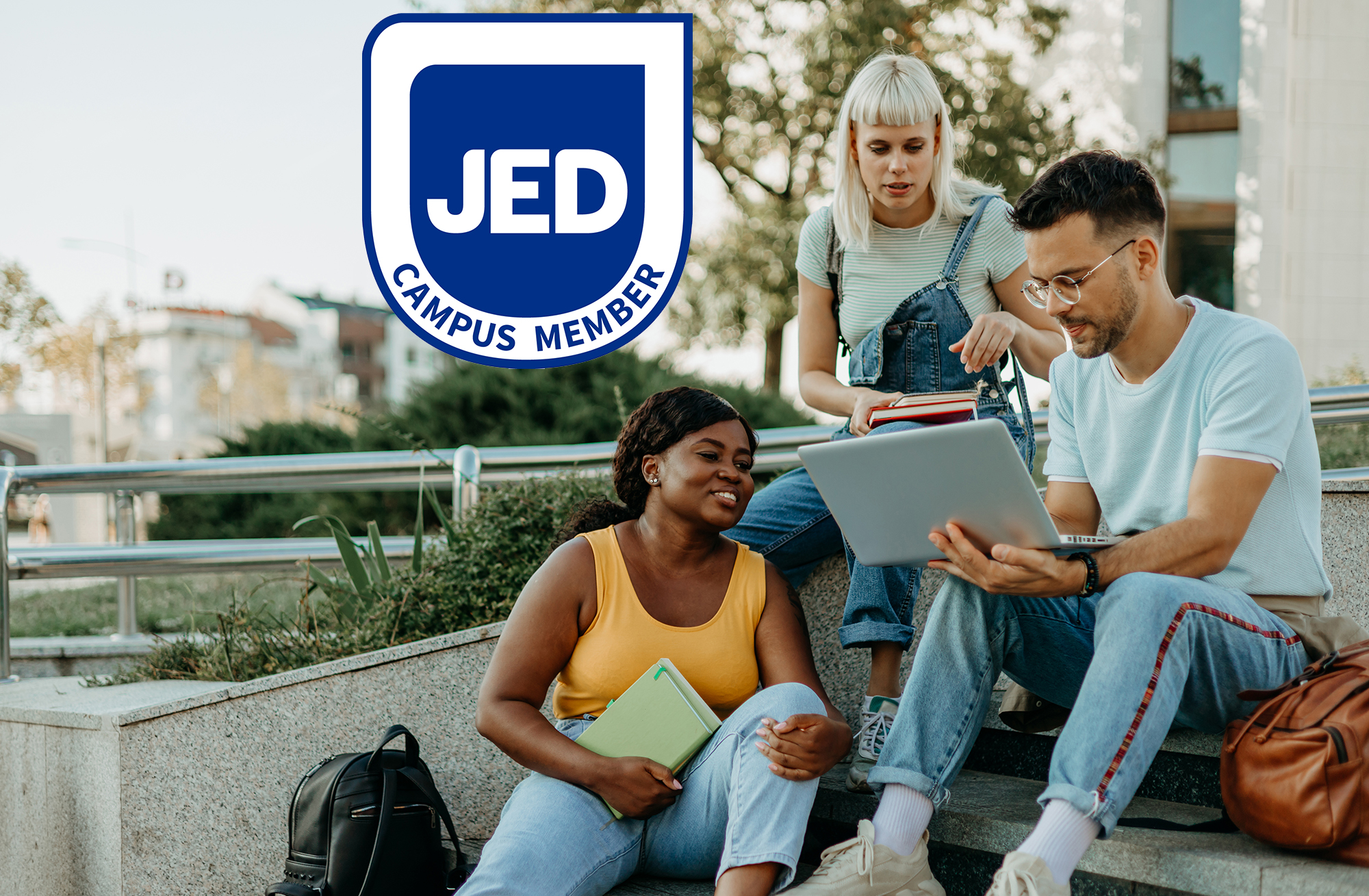 Group of students sitting on the steps of a building, the JED Campus logo is to the left.