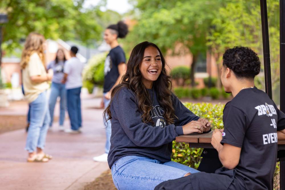group of students at table and standing on UNC Pembroke campus sidewalk