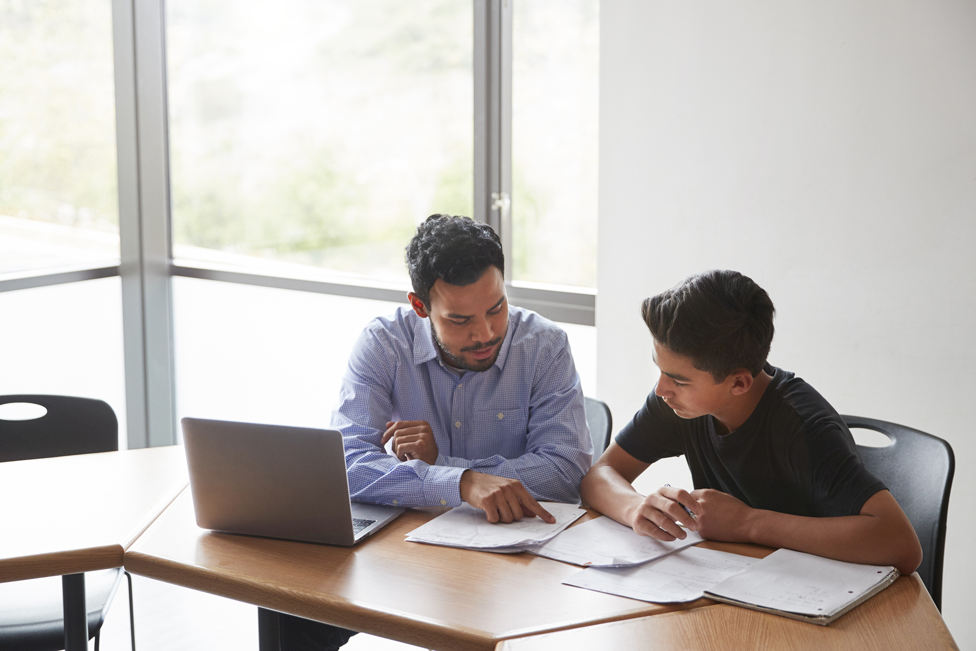 man and college student sitting at paperwork and computer