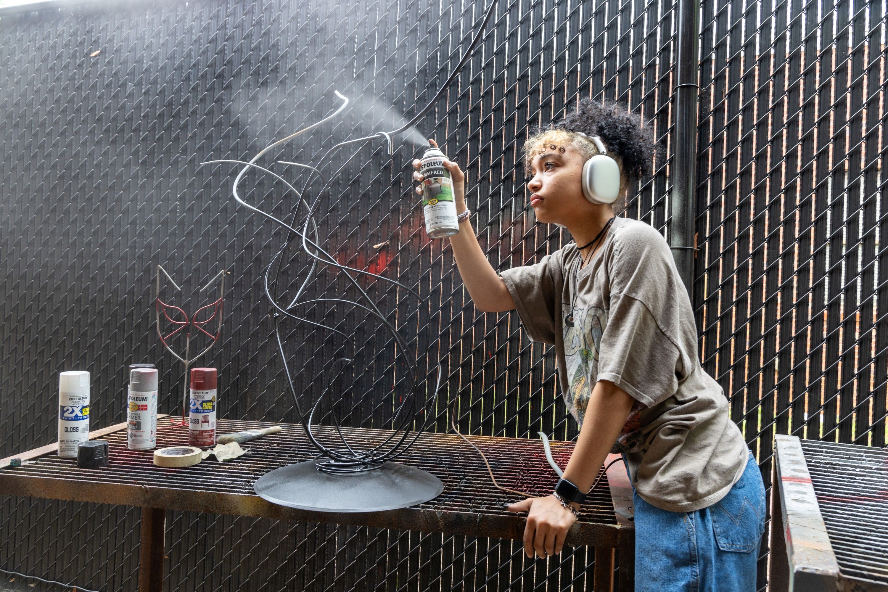 Sculpture student wearing headphones spray painting her metal sculpture in the outdoor portion of the sculpture studio at UNC Pembroke.