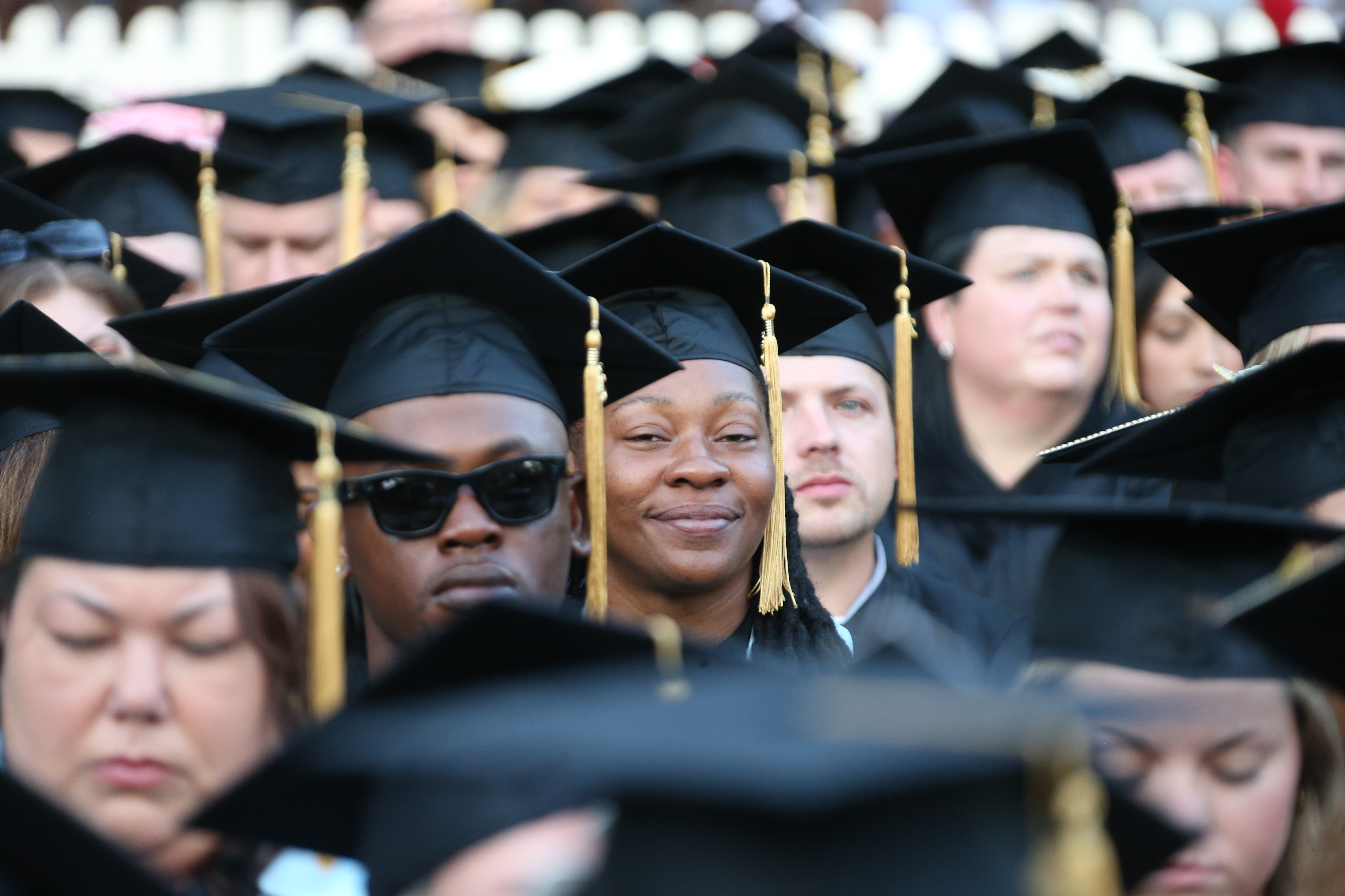 A group of graduates in black caps and gowns seated closely together, with their faces blurred.